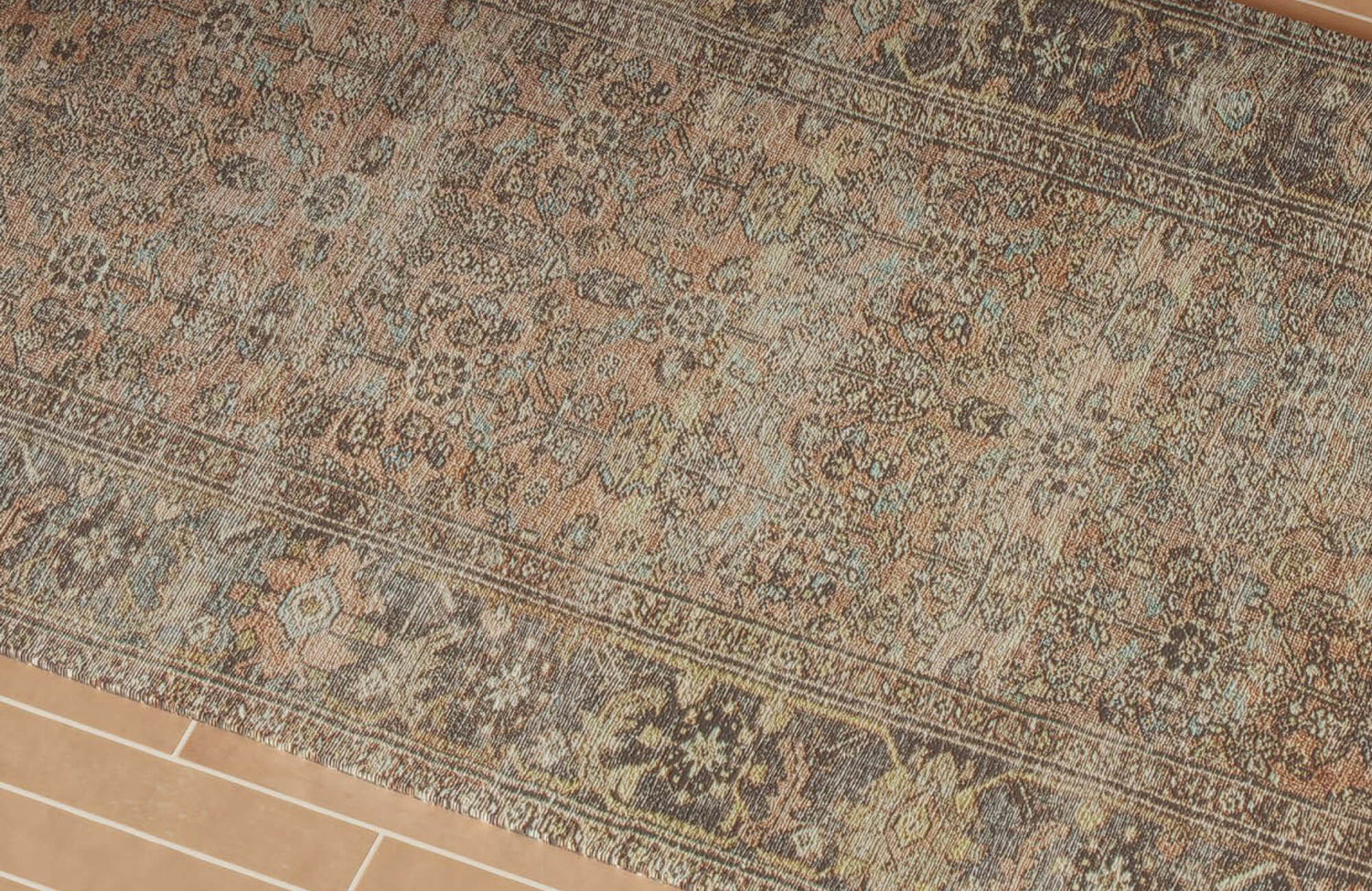 Vintage-inspired area rug featuring intricate medallion motifs in muted spice, indigo, and earthy brown tones, styled beside warm terracotta tile flooring and woven natural-fiber décor.