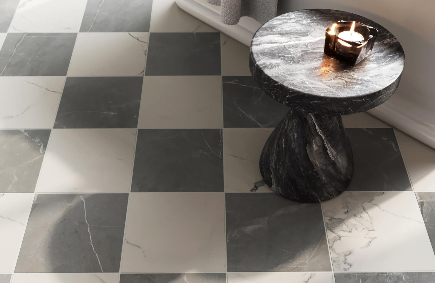 Black and white marble checkerboard floor paired with a sculptural stone side table, topped with a lit candle for a warm modern accent.