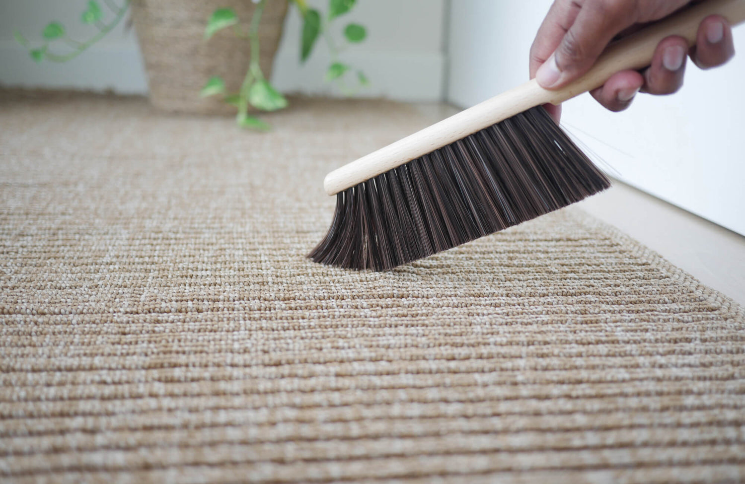 A hand brushing debris from a natural woven rug, highlighting simple maintenance and low-allergen rug care.