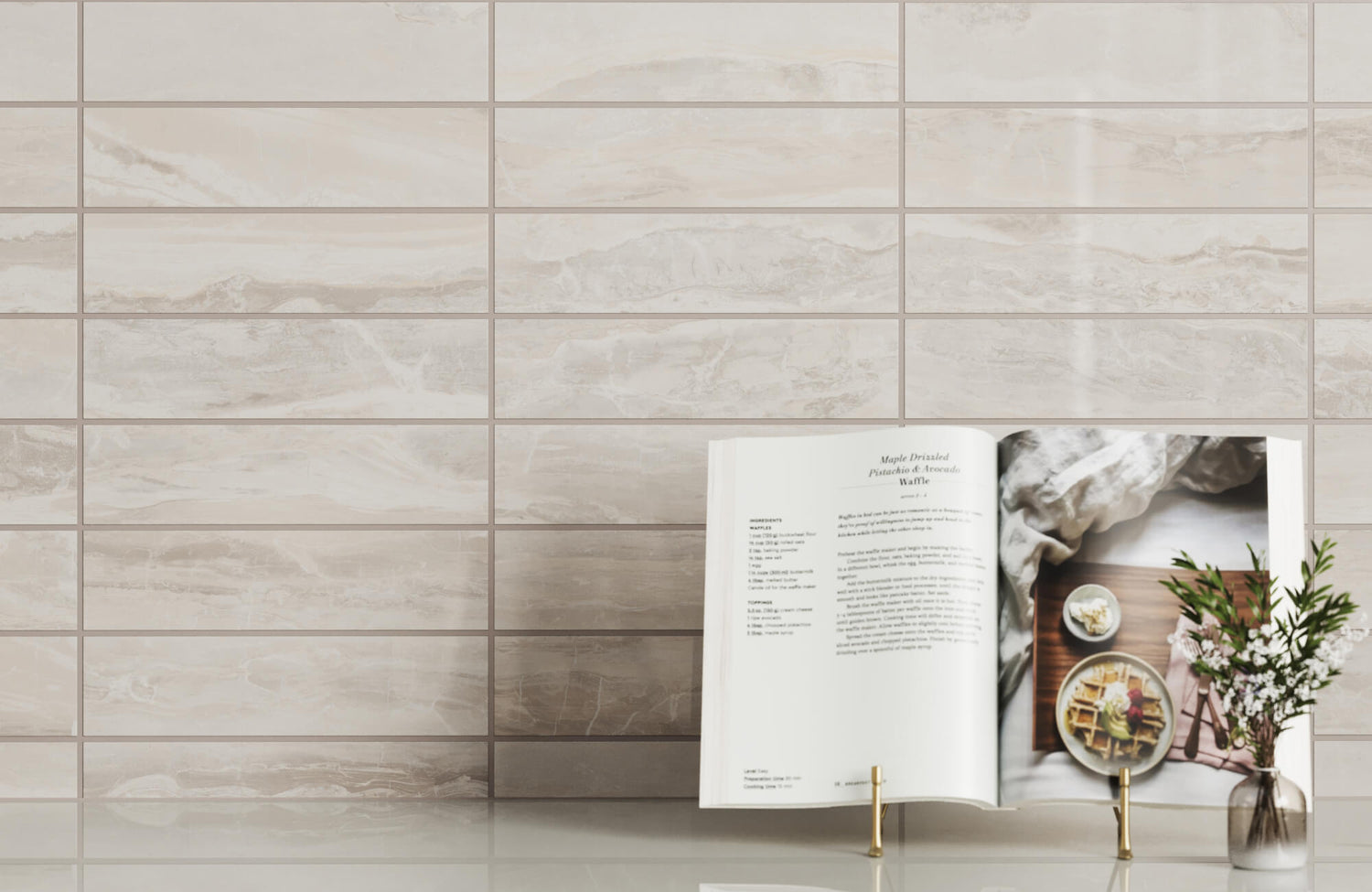 Elegant 3x12 grayish beige porcelain tiles with soft marble-like veining create a serene backdrop, complemented by an open cookbook and a vase with fresh flowers on a sleek countertop.
