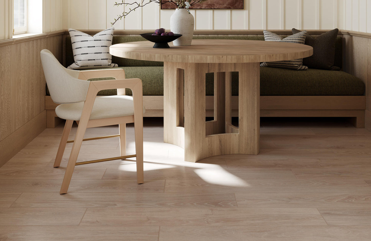 Soft beige wood look tiles bring a natural feel to this cozy dining nook, pairing with a round wood table, built-in bench seating, and a cream accent chair.