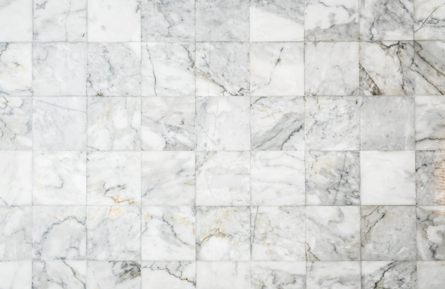 White marble tiles arranged in a grid pattern with soft gray veining and natural stone variation across the polished surface.