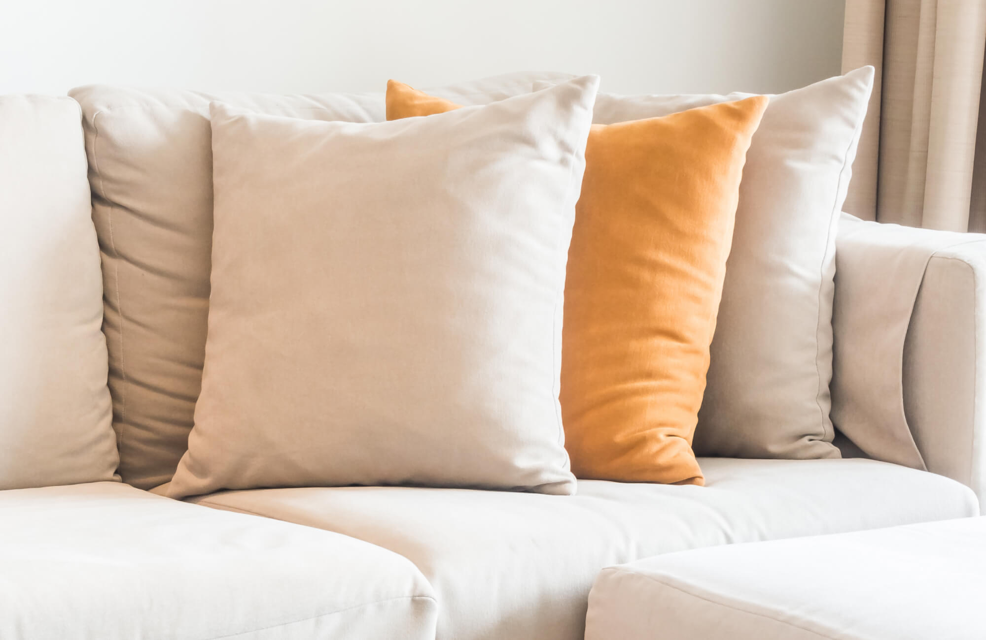 Orange and beige throw pillows arranged on a neutral upholstered sofa in a minimalist living room.