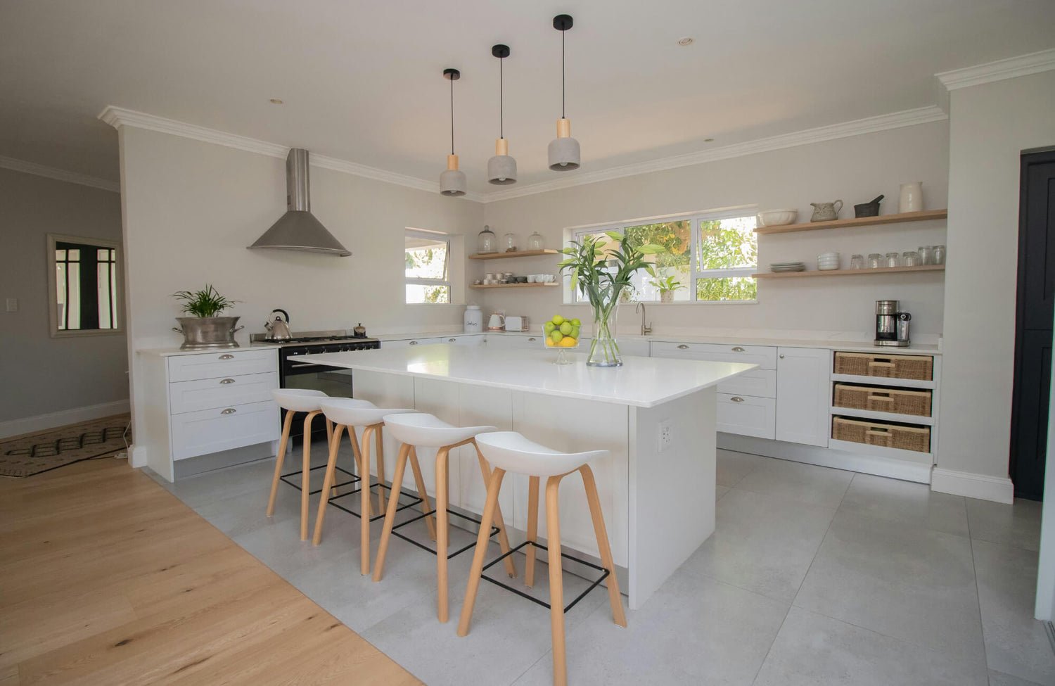 Bright modern kitchen with a large white island and four minimalist white bar stools with wooden legs.
