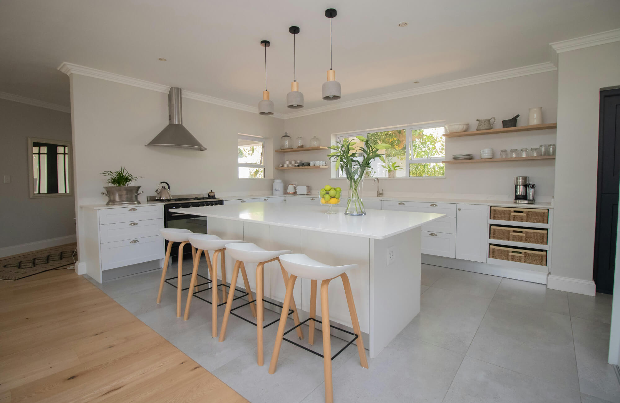 Bright modern kitchen with a large white island and four minimalist white bar stools with wooden legs.