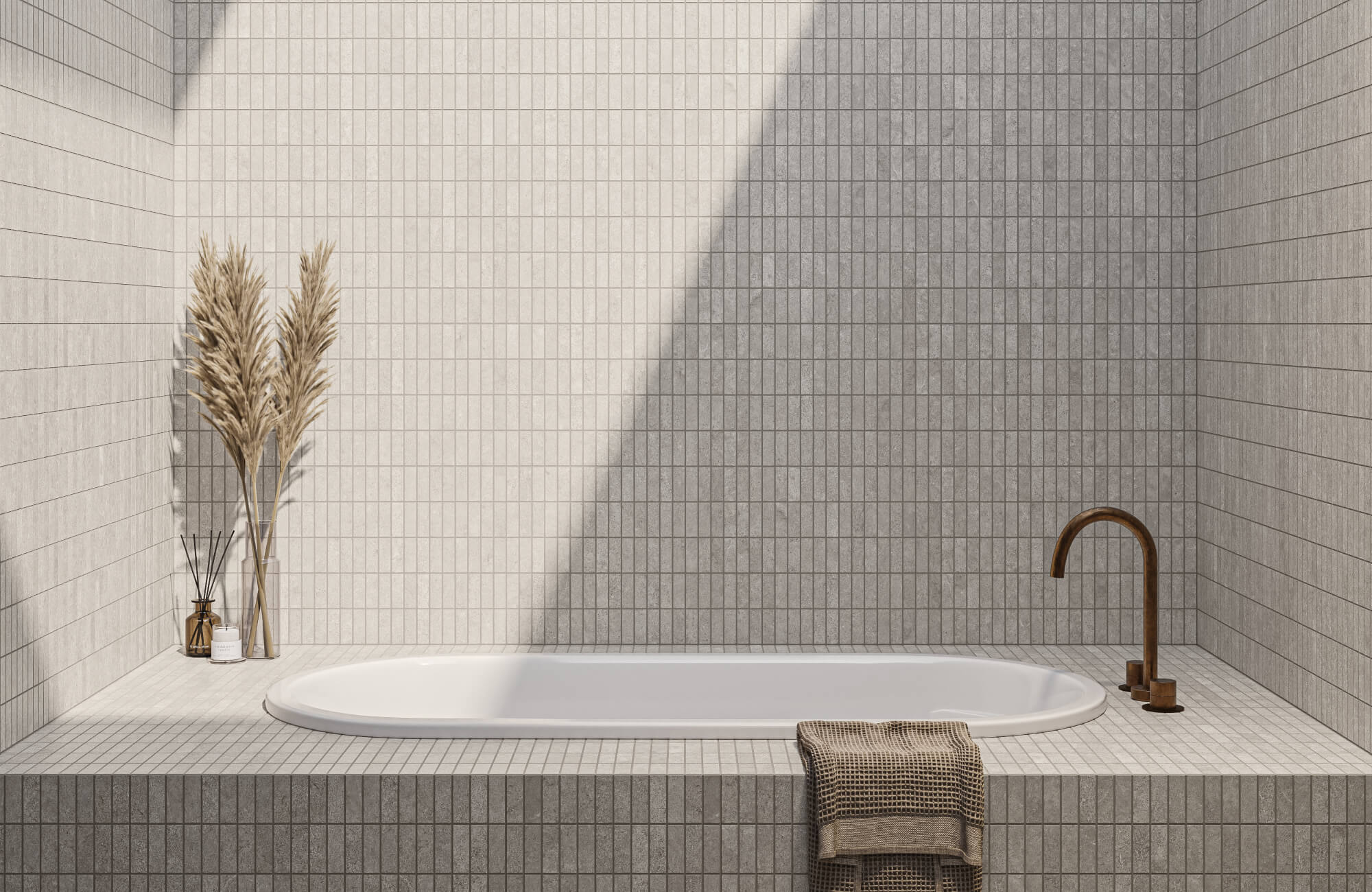 Neutral bathroom with small stacked mosaic tiles around a built-in bathtub, beige and gray wall tile panels, a bronze floor-mounted faucet, dried pampas grass, and a textured towel.