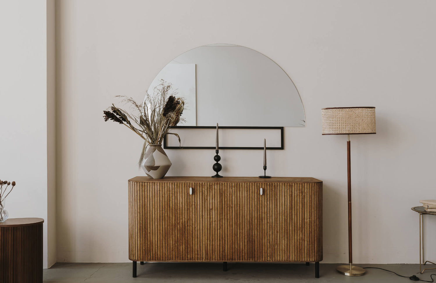 Wooden sideboard with a large half-round mirror, dried florals, and candles styled against a soft neutral wall.