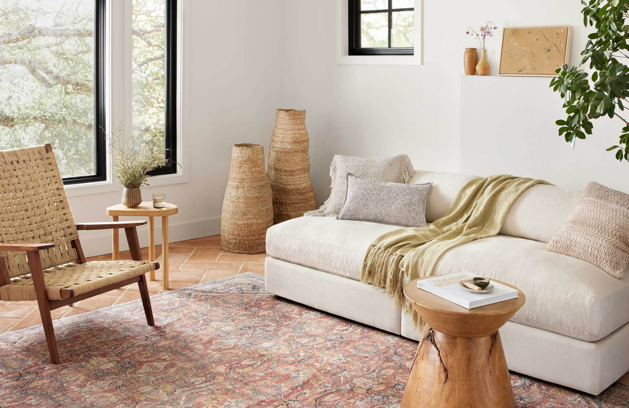 Neutral living room with a cream sofa styled with layered textured throw pillows, woven accent chair, patterned rug, and warm natural decor accents.