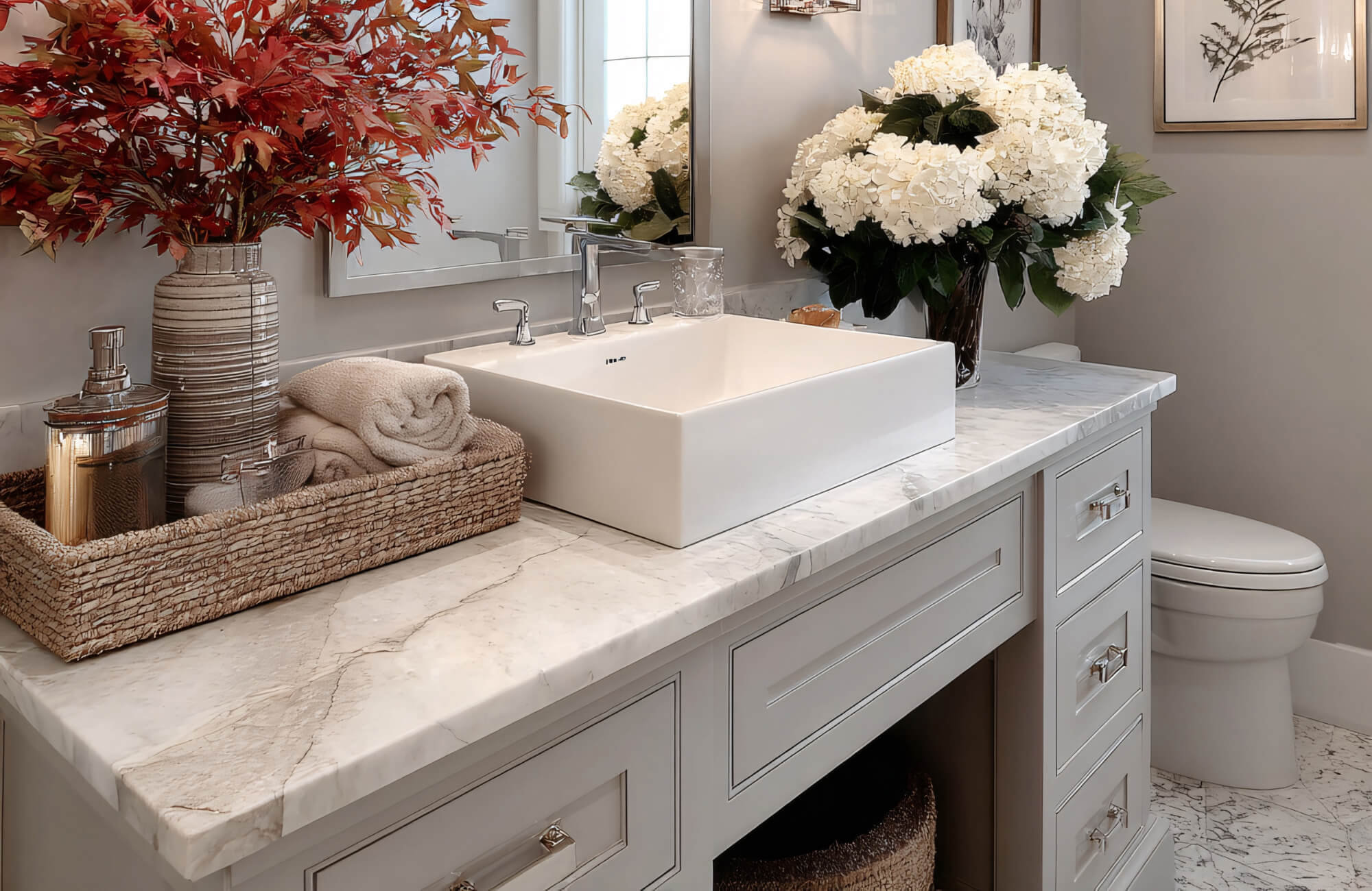 A marble bathroom vanity with a vessel sink, decorative trays, and floral arrangements creating an elegant, styled countertop.