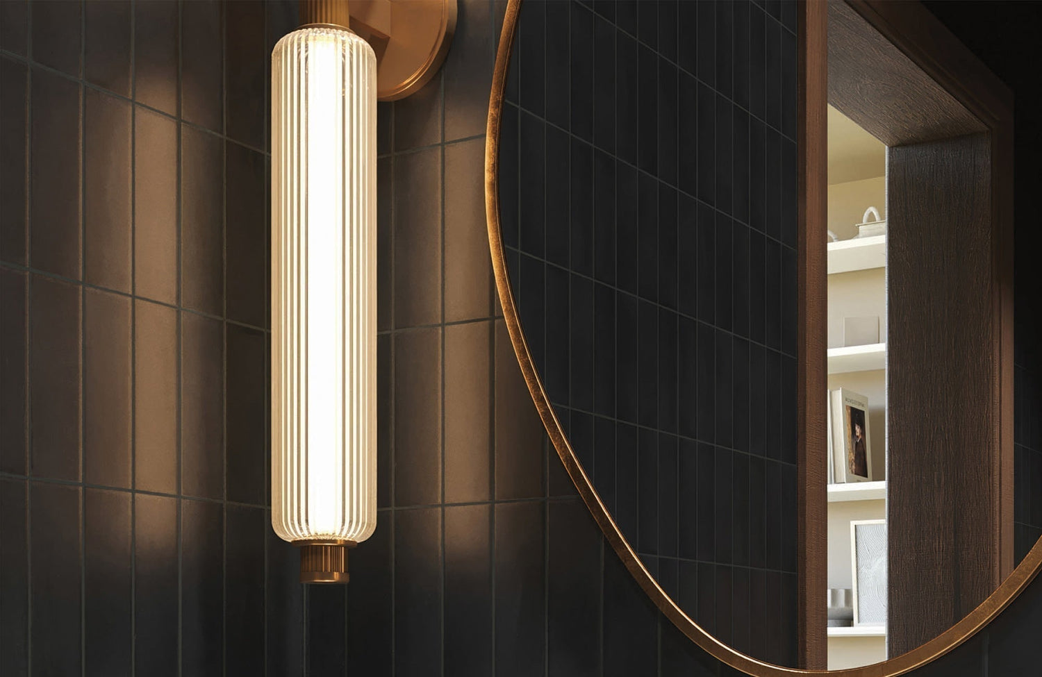 Vertical ribbed sconce glows beside a round mirror in a modern bathroom with dark tile and warm wood accents.