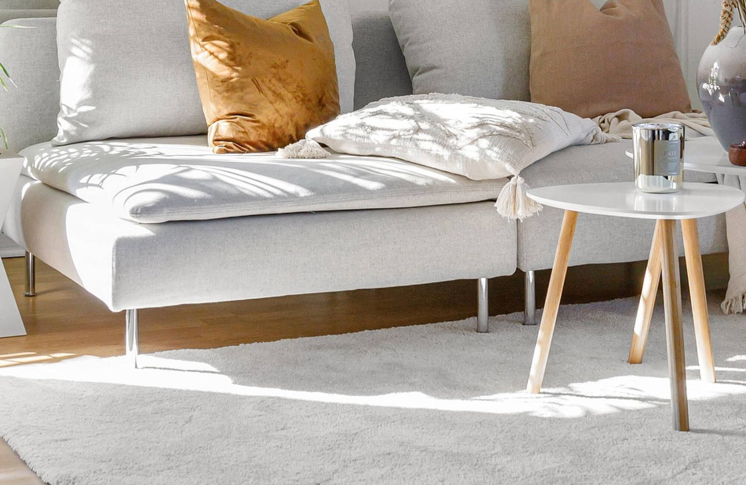 Bright modern living room with a soft white wool rug anchoring a minimalist sofa and neutral-toned pillows, creating a warm, inviting, and elegant atmosphere.