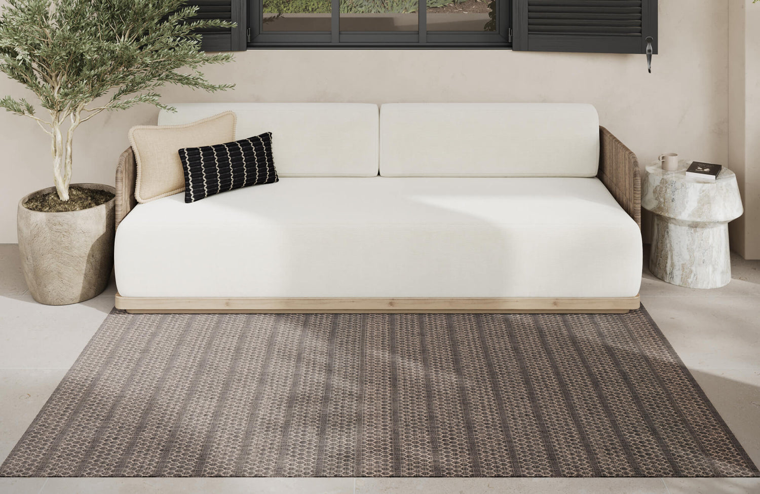 Patterned outdoor rug in layered brown tones styled under a neutral daybed, illustrating how durable synthetic fibers complement sheltered patio spaces.