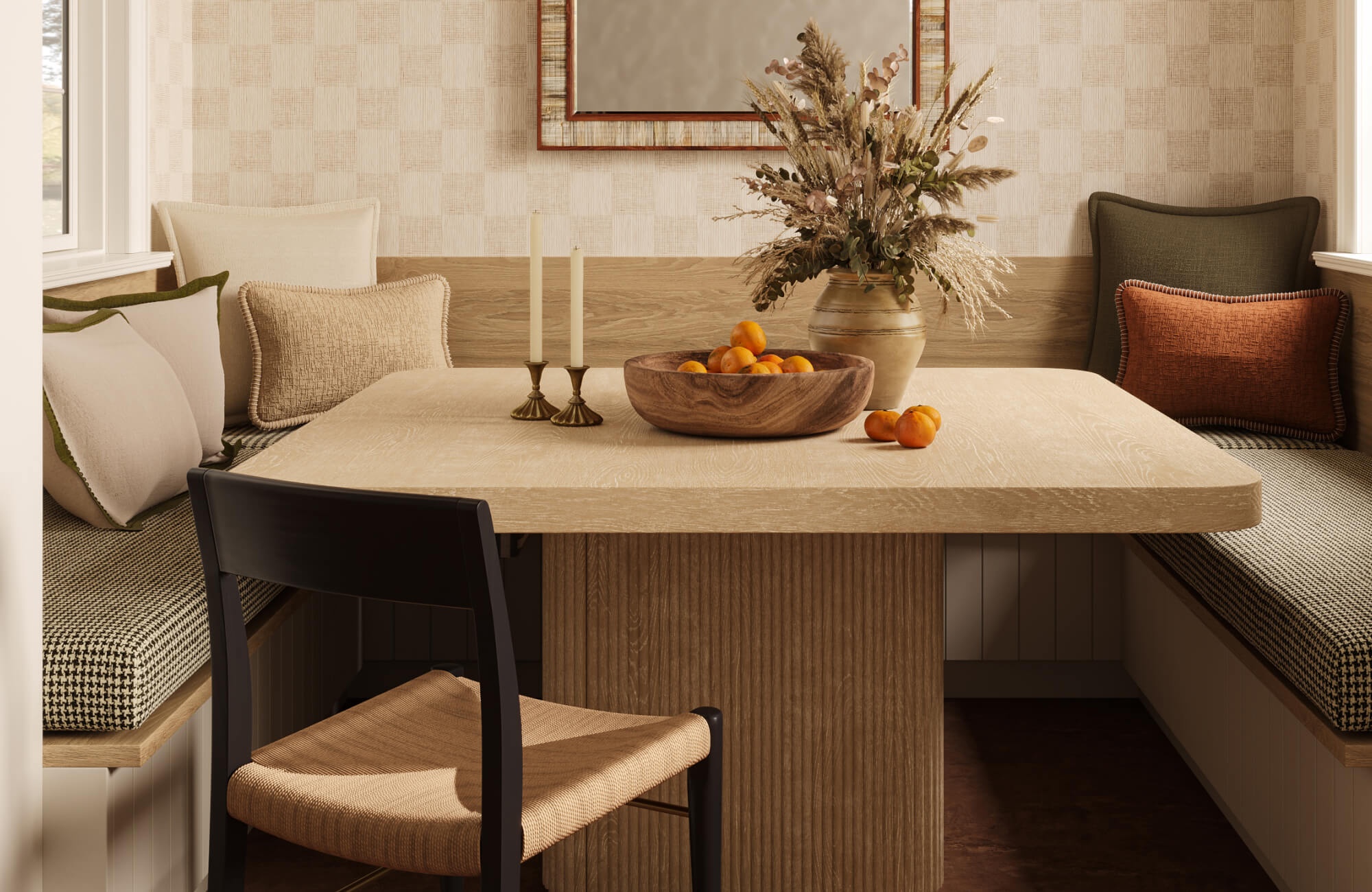 Cozy breakfast nook with a light wood pedestal table, built-in banquette seating, and decorative pillows in cream, olive, beige, charcoal, and rust tones for an earthy, layered dining space. 
