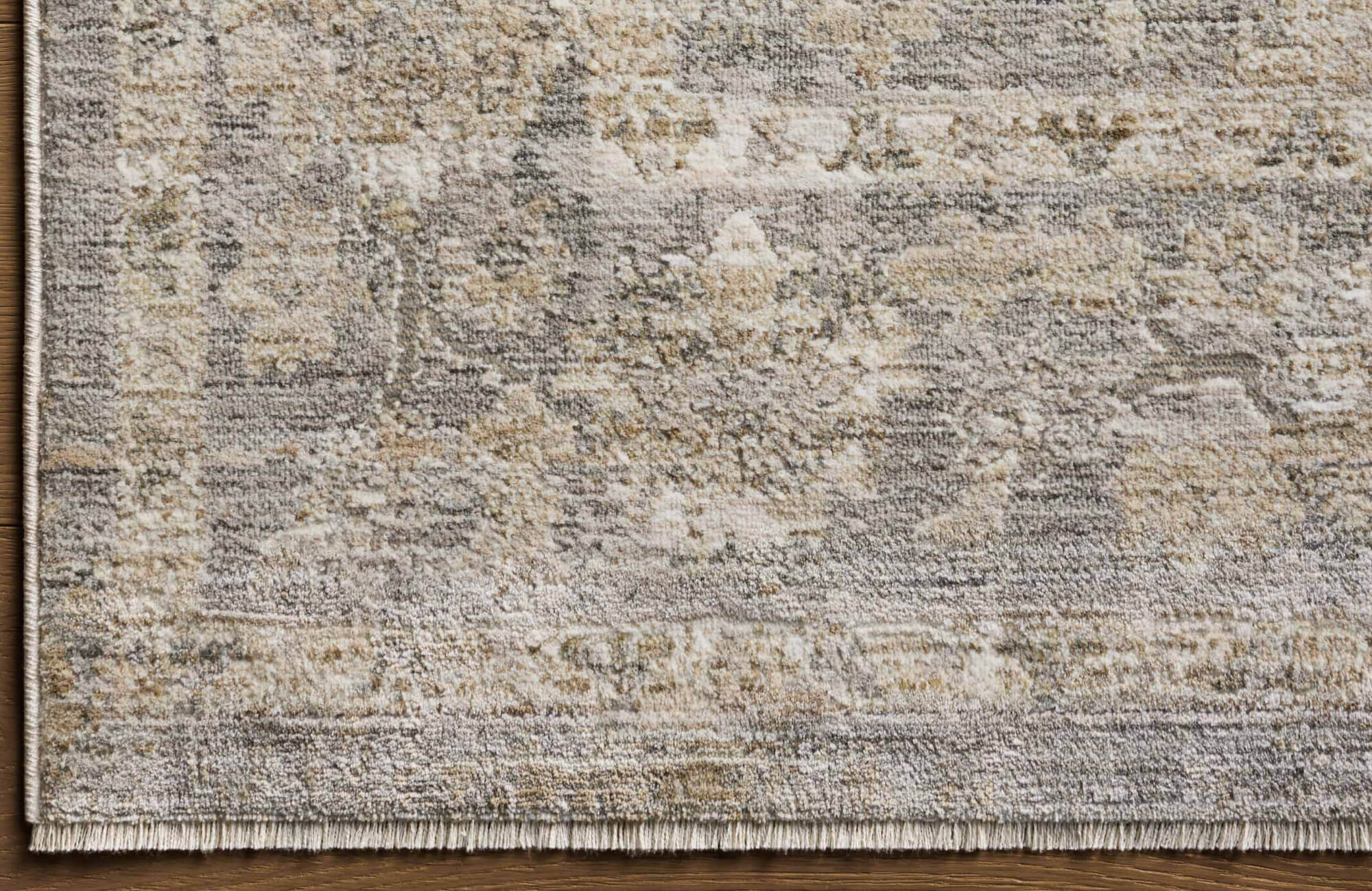 Textured area rug in muted beige, cream, and grey tones with a distressed, vintage-style pattern and subtle fringe edge.