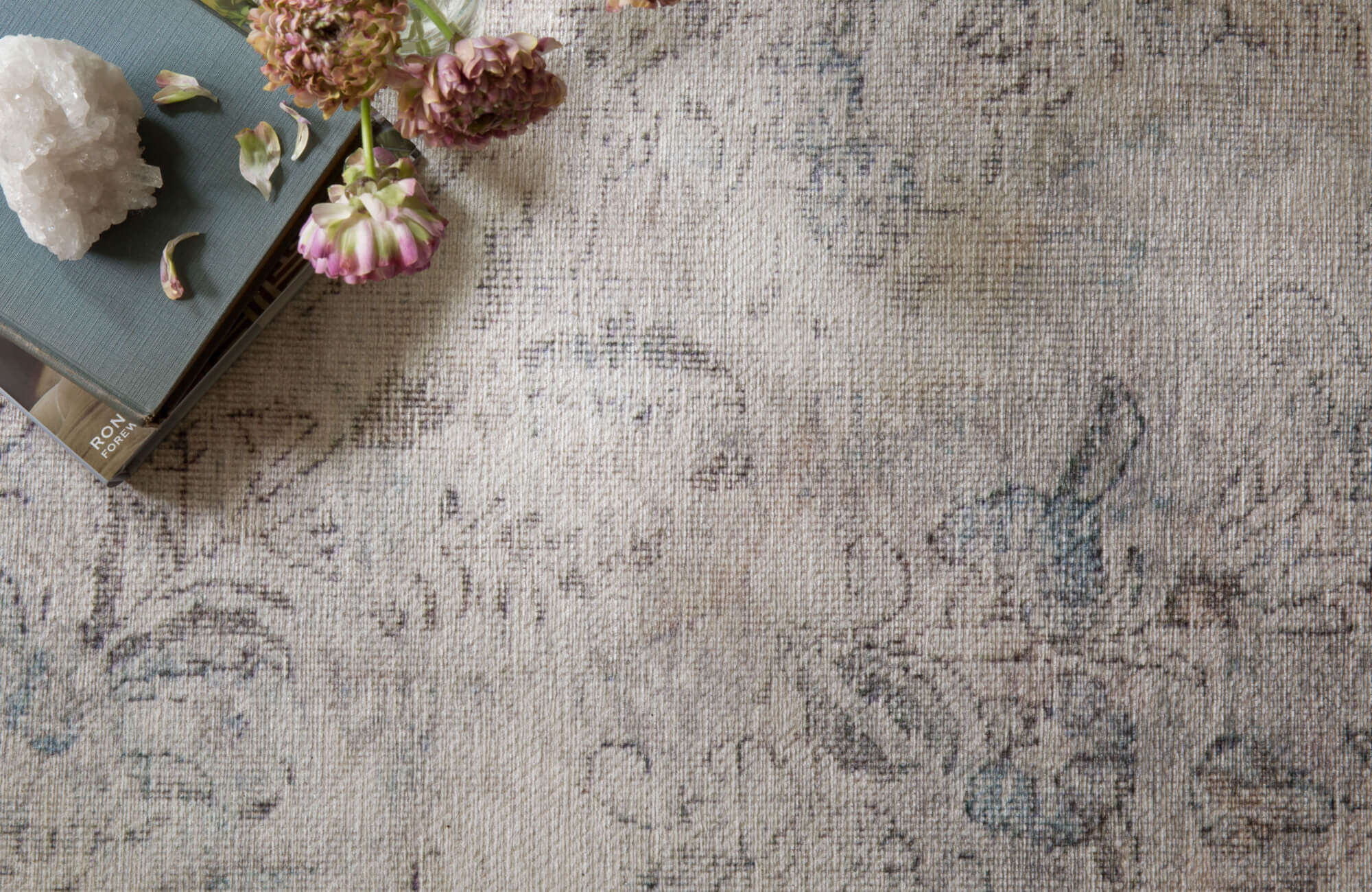 Subtle floral-patterned rug in soft taupe and faded blue tones, evoking a vintage, timeworn elegance.