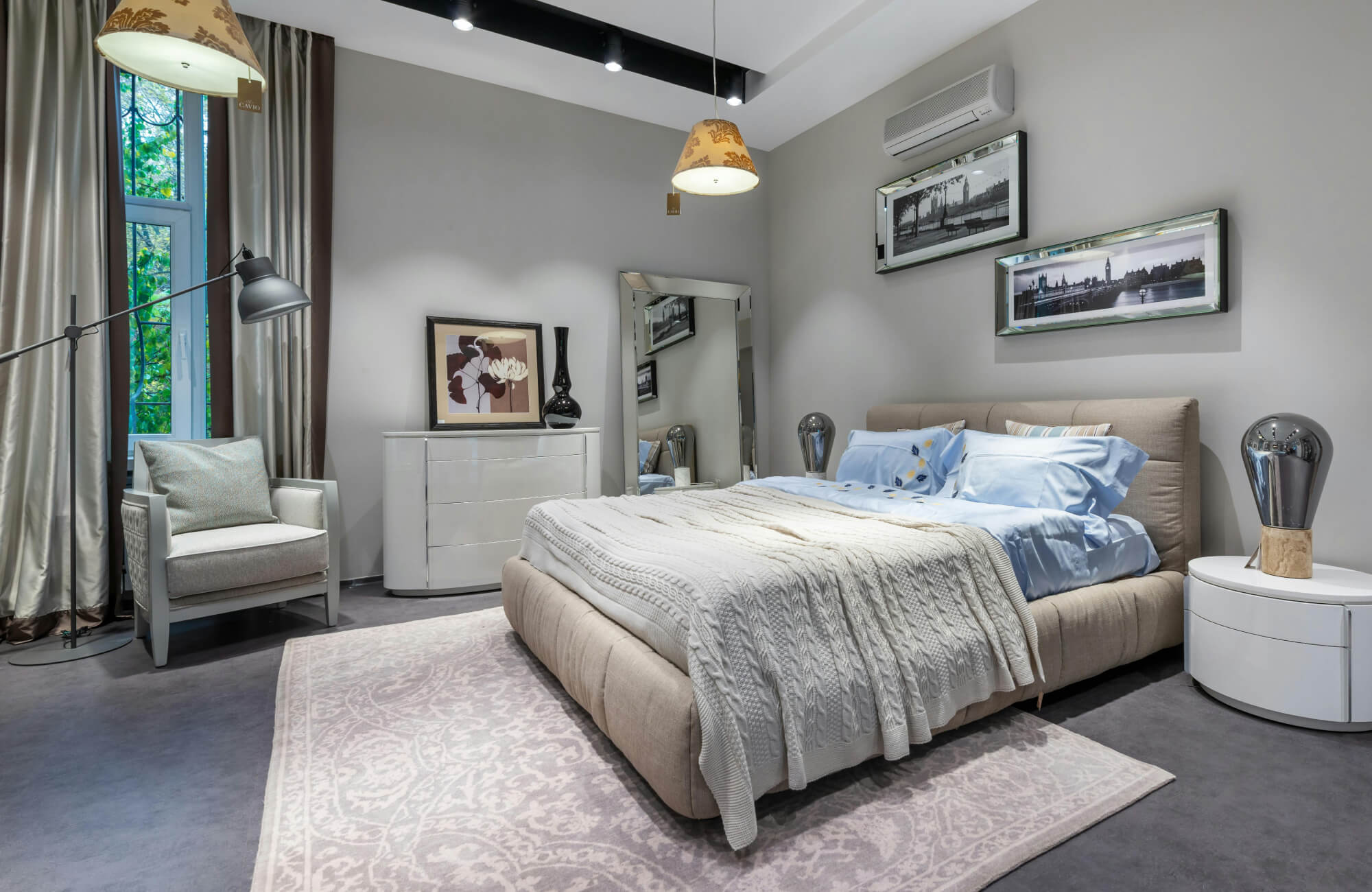 Modern bedroom with soft gray walls, a tufted beige bed, and layered textures including a knit throw and patterned rug.