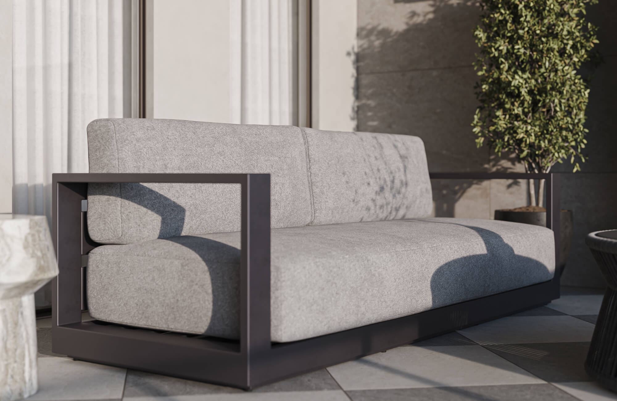 Contemporary outdoor patio featuring a modern gray cushioned sofa with a black geometric metal frame, checkerboard tile flooring, sculptural side tables, and surrounding greenery in a minimalist open-air setting.