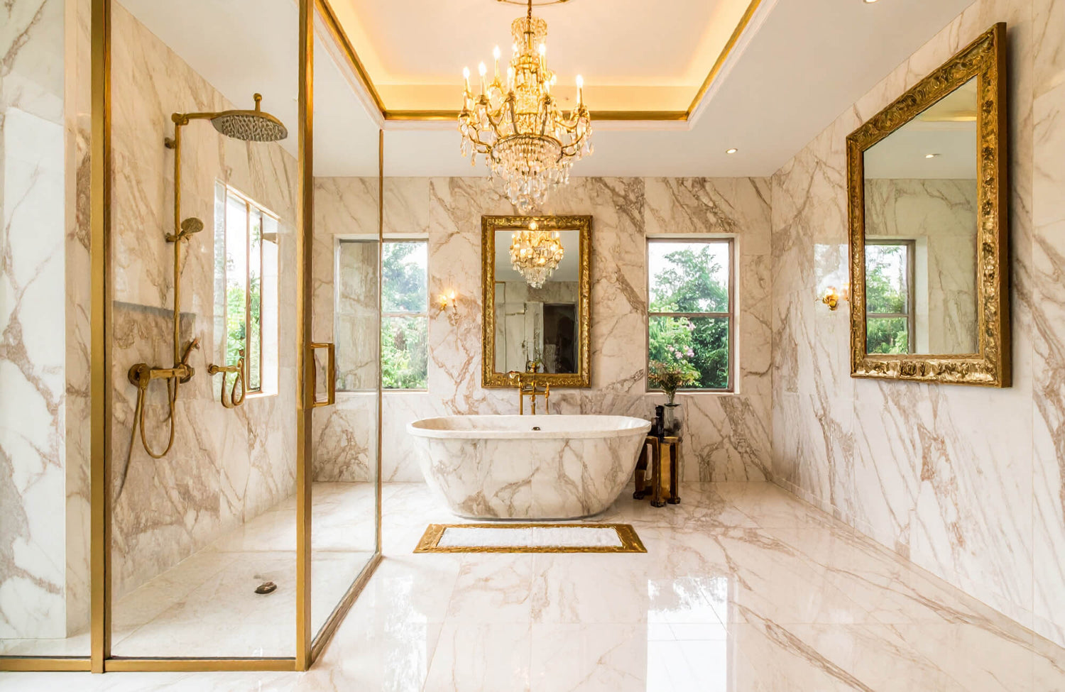 A luxurious marble bathroom featuring gold-framed mirrors, a freestanding tub, gold fixtures, and a crystal chandelier.