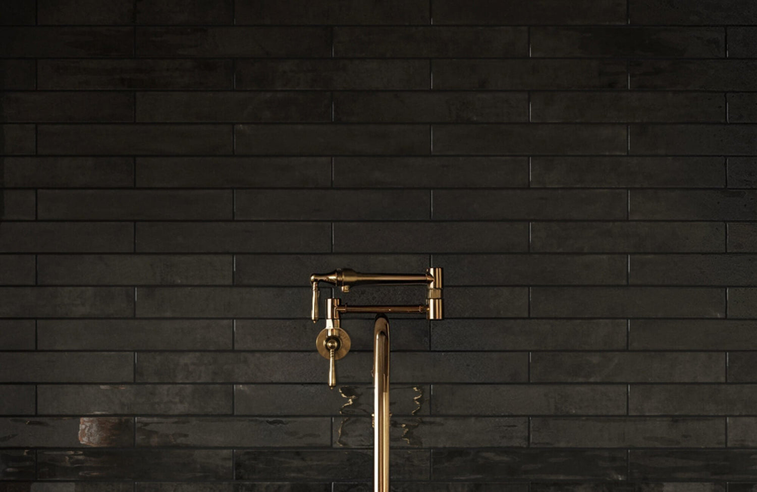 Sleek black subway tile backsplash with a mix of matte and gloss finishes highlights a striking brass pot filler faucet.