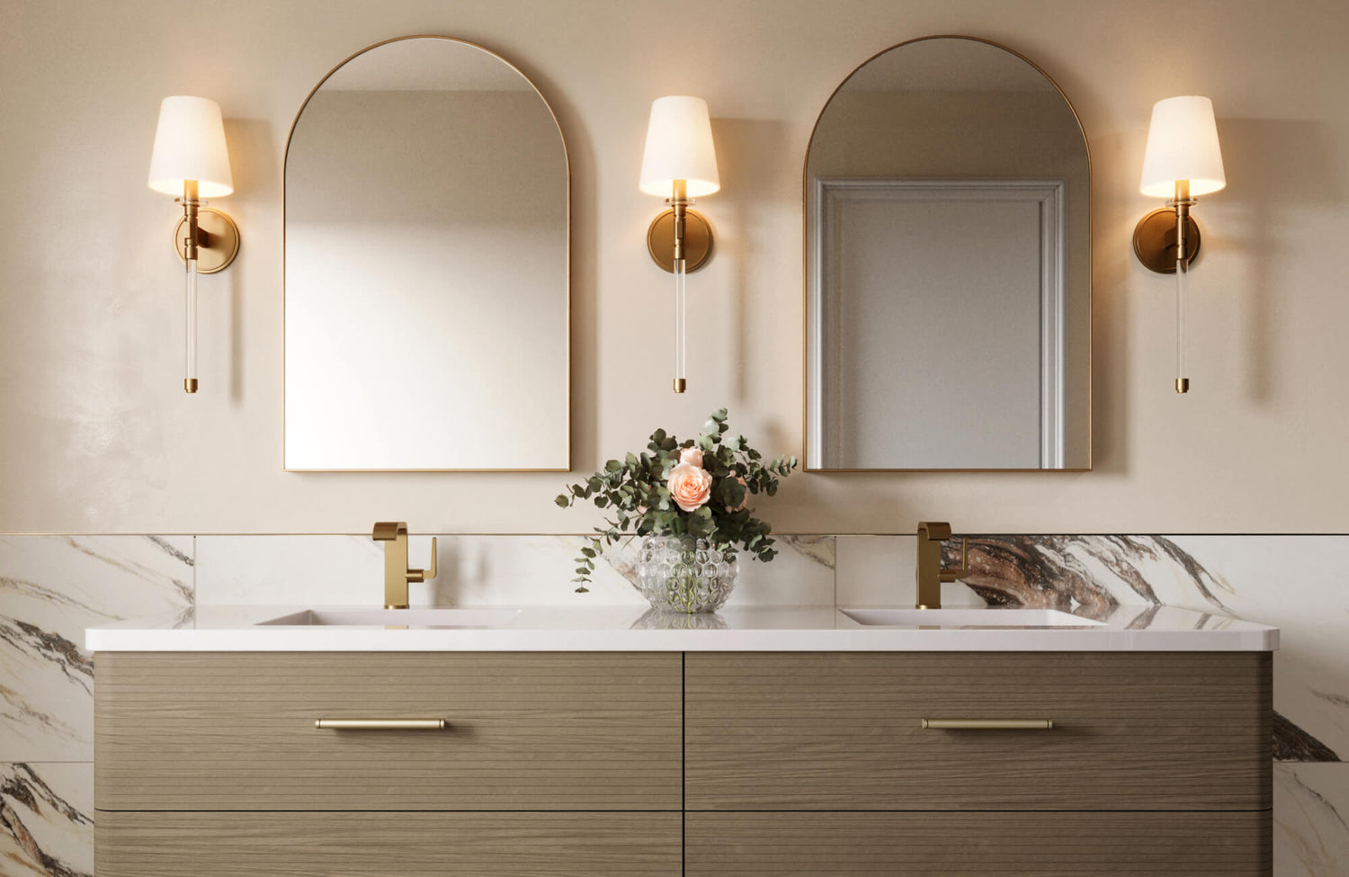 Double vanity with brass faucets, arched mirrors, and warm wall sconces, set against a marble look tiled backsplash.