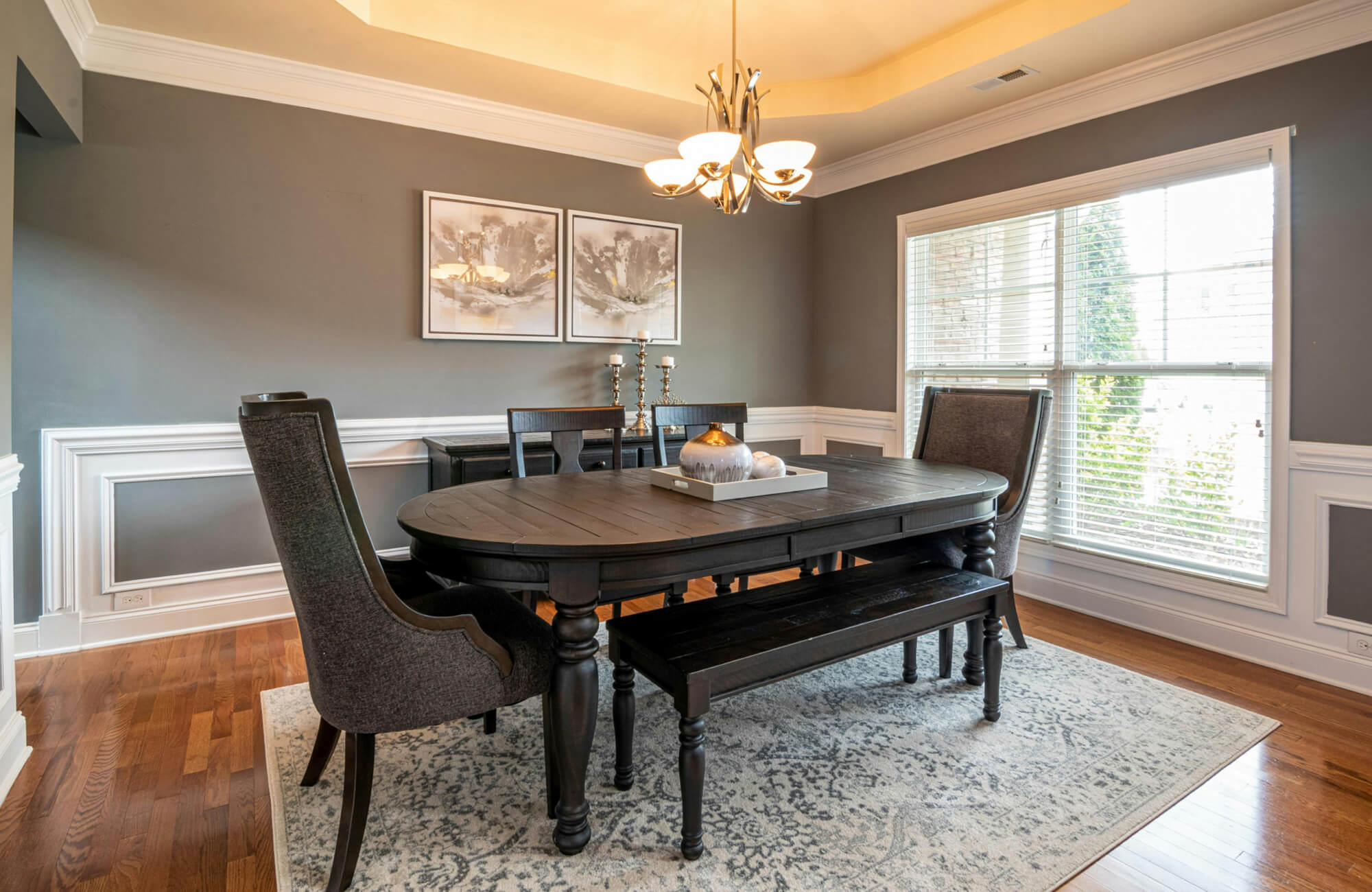 Traditional dining room with a dark wood table, upholstered chairs, and a patterned area rug over warm hardwood flooring.