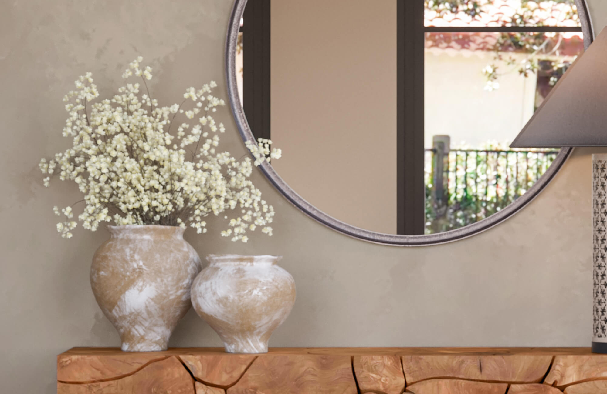 Vase with rounded ceramic silhouette holding white baby's breath branches on a wooden console table beneath an arched mirror.