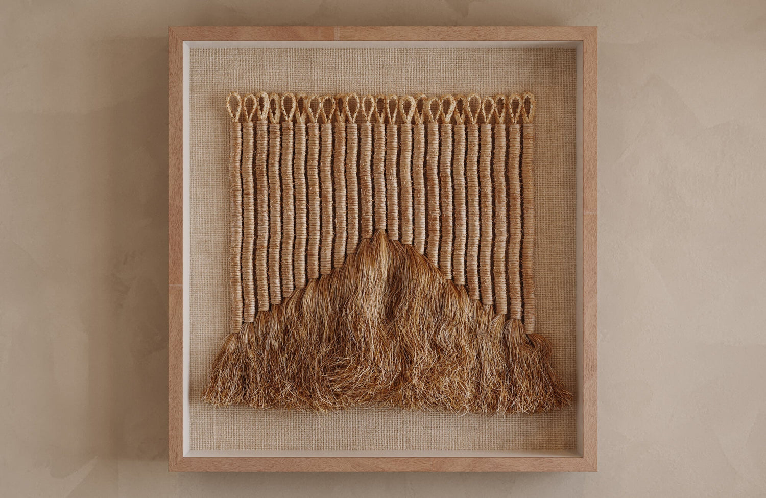 Contemporary fiber art piece with looped cord detailing and layered straw-like strands, displayed against a beige wall in a simple wooden frame.