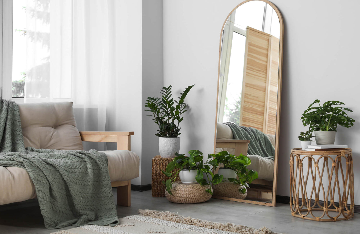 Cozy living room with a full-length arched mirror, indoor plants, and a neutral-toned sofa draped with a green knit throw blanket.