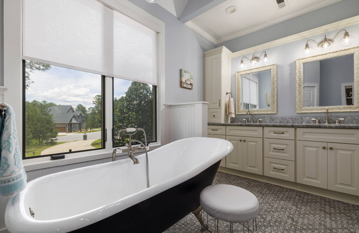 Elegant bathroom with freestanding black-and-white tub, double vanity with framed mirrors, and large window with outdoor view.