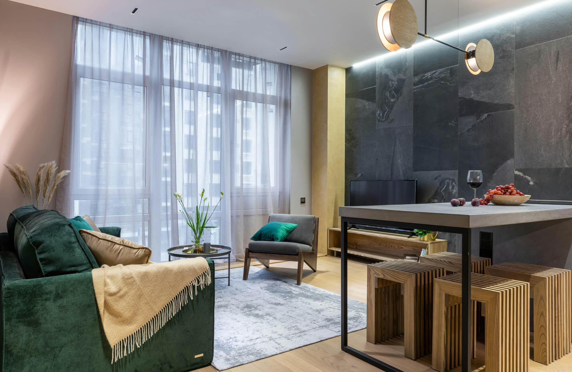 Modern open-plan living space with a gray area rug, emerald green sofa, and wood-accent furniture creating a cozy, contemporary atmosphere.