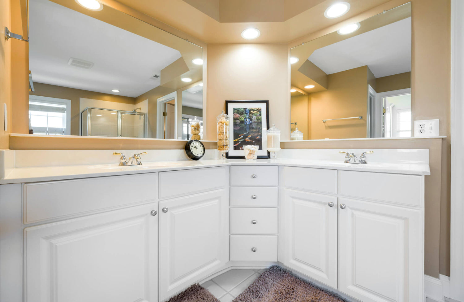 A corner vanity bathroom layout with white cabinetry, dual mirrors, and warm brass lighting that shows how angled vanities can maximize wall space in smaller bathrooms.
