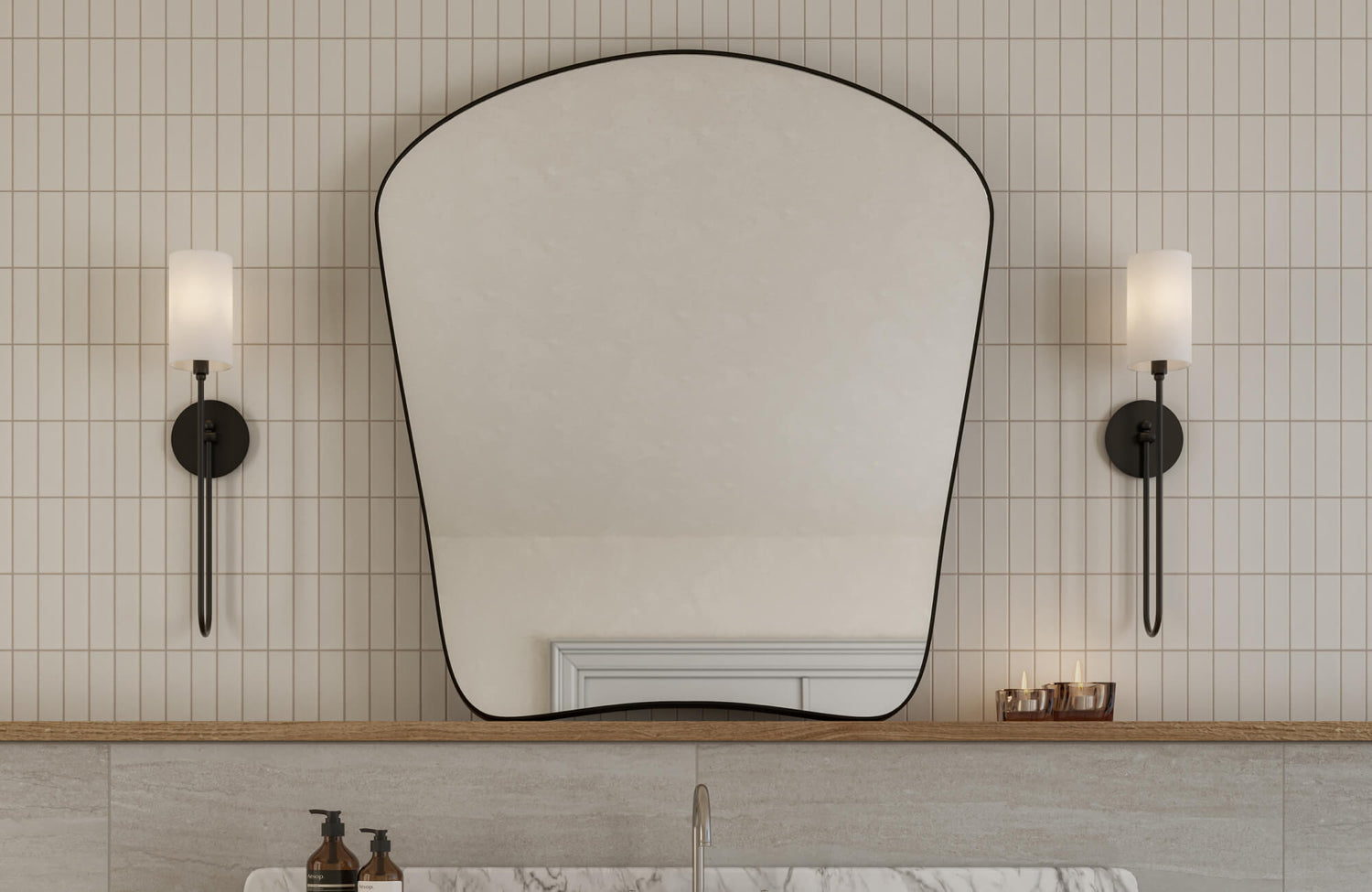 Arched mirror with a slim black frame, flanked by modern wall sconces, set against vertical, straight lay cream tiles in a chic bathroom.