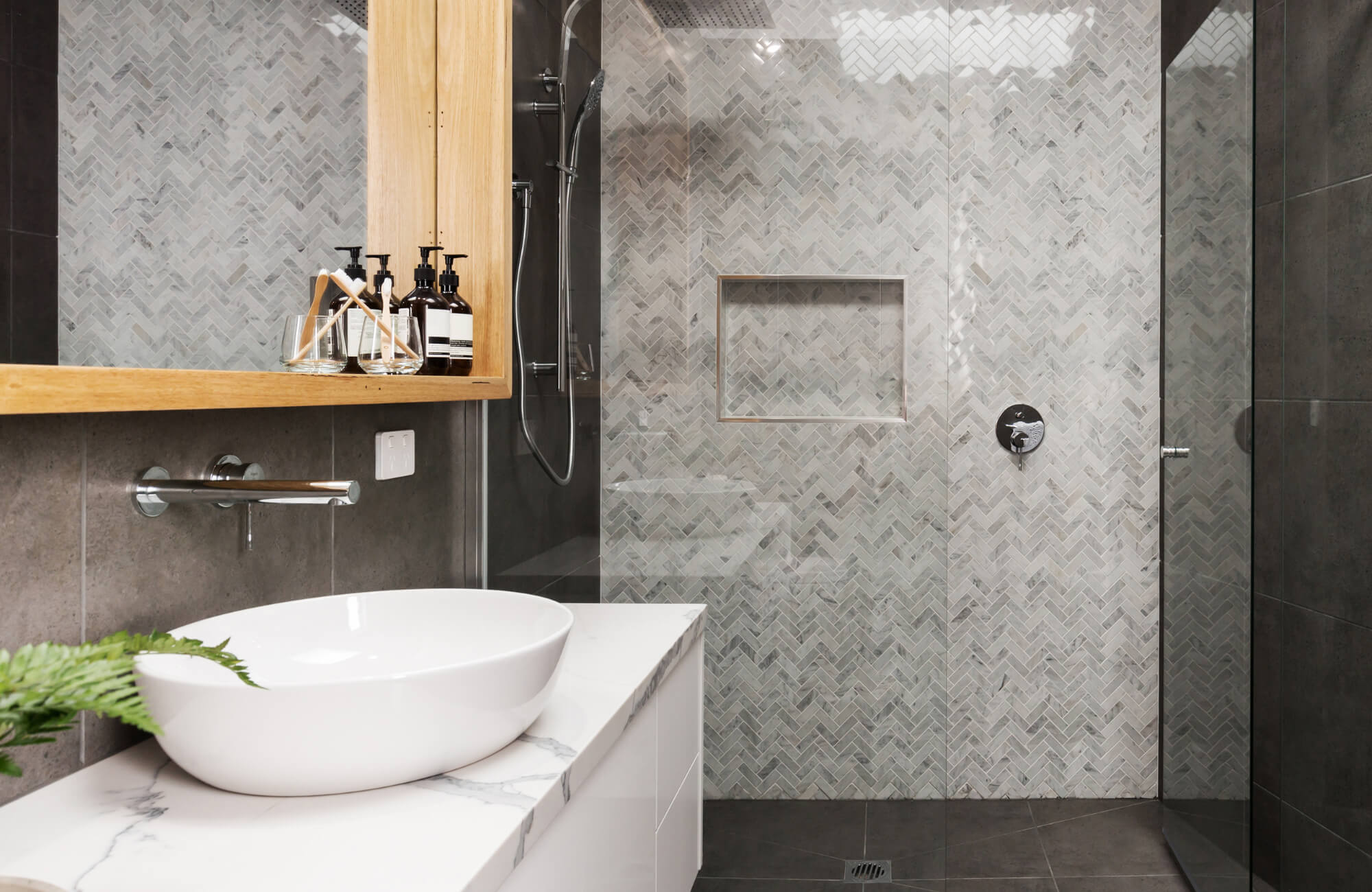 Modern bathroom with a herringbone mosaic shower wall, built-in niche, vessel sink, and wood accents for a sleek, spa-like look.