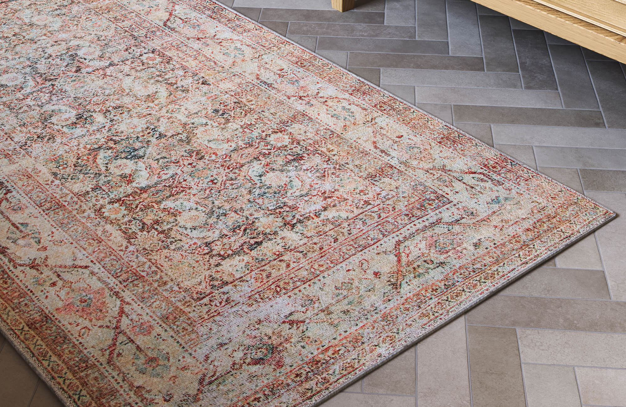 Herringbone-patterned cement look tiles in warm grey tones paired with a vintage-style rug rich in earthy reds and soft pastels.
