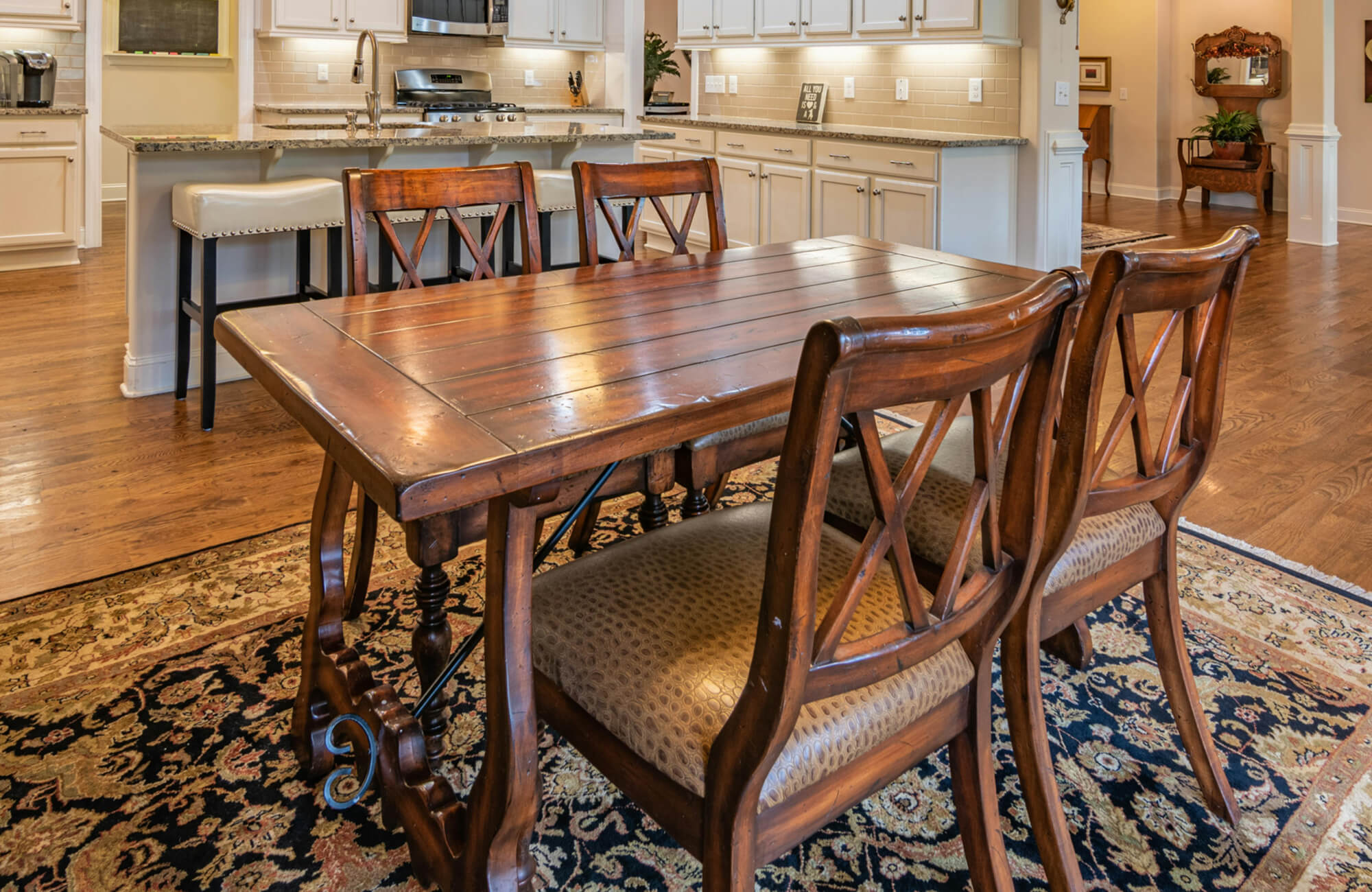 Traditional dining space with a carved wood table, cushioned chairs, and a rich floral-patterned rug over warm hardwood floors.