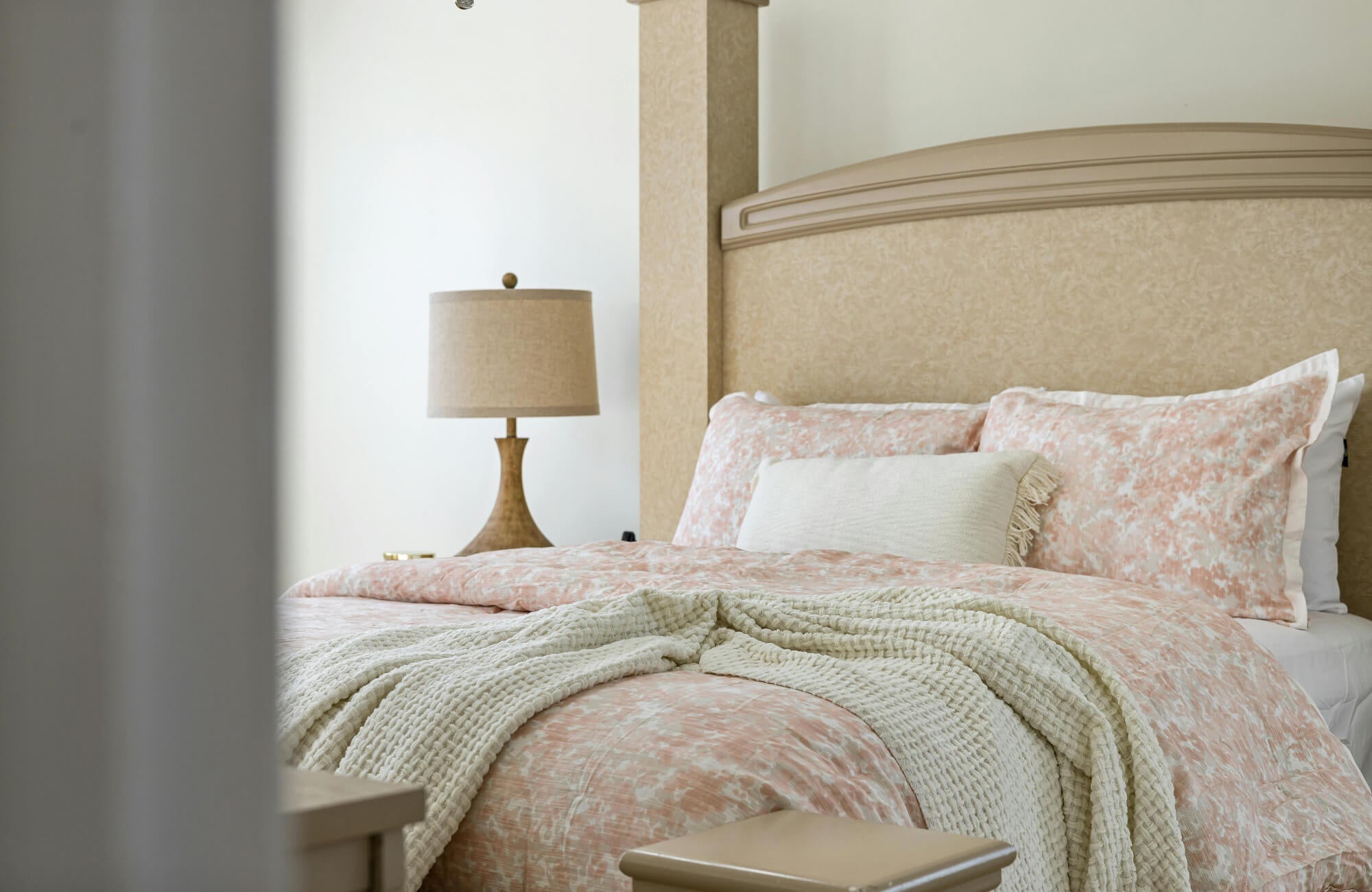 Pink patterned pillow shams arranged upright on a bed with matching bedding, a cream throw blanket, and a neutral upholstered headboard.