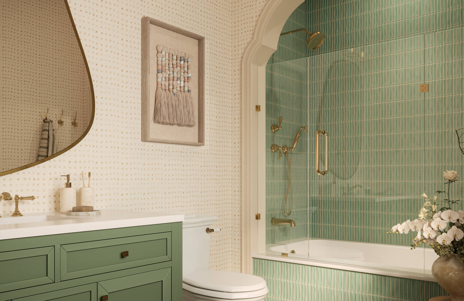 A woven wall art piece softens this bright bathroom, complementing cream wallpaper, muted sage cabinetry, and glossy aqua green tile for a layered, inviting look.