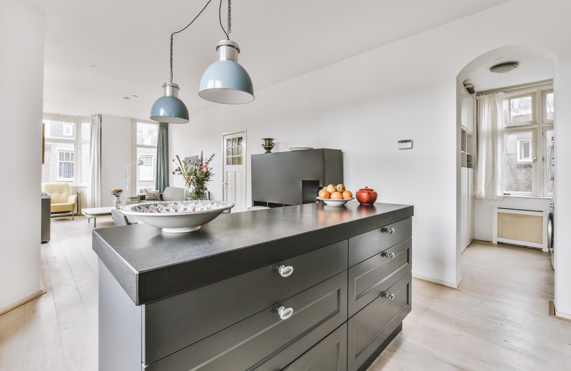 Modern open-concept kitchen with a black island, pendant lighting, and light wood floors, connecting to a bright living area.