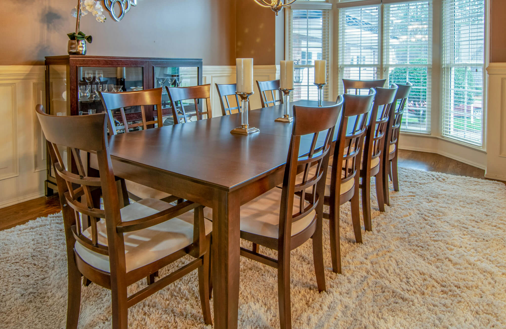 A sun-filled dining nook features an elegant patterned large rug that grounds the dining set, softens the hardwood floors, and enhances the airy feel created by the surrounding floor-to-ceiling windows.