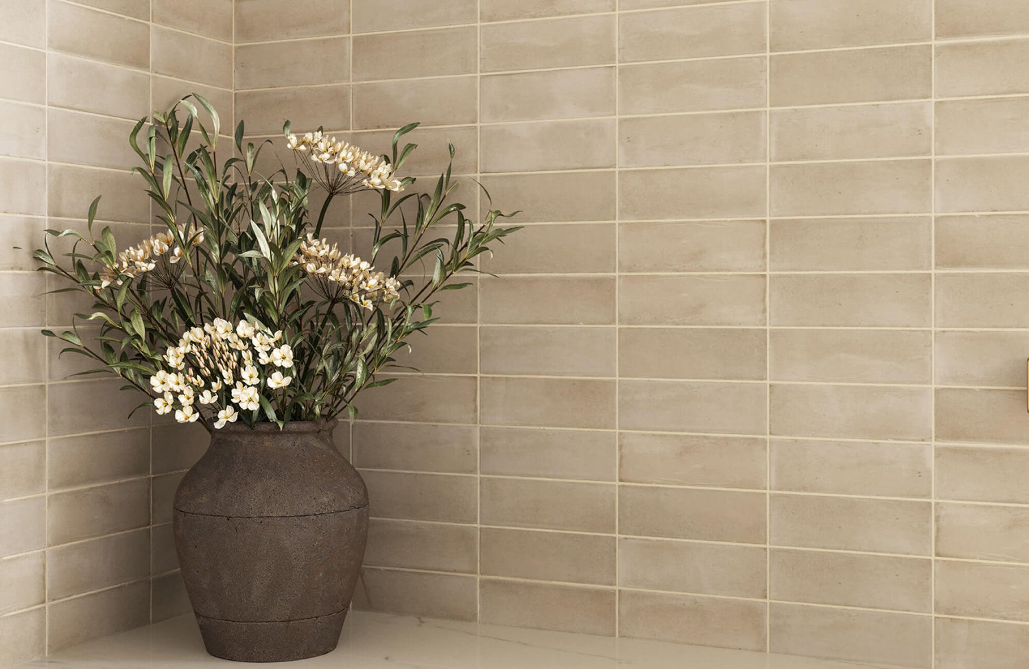 Beige subway tile wall in a kitchen corner with soft tonal variation, white grout, a marble countertop, and a dark ceramic vase with flowers.