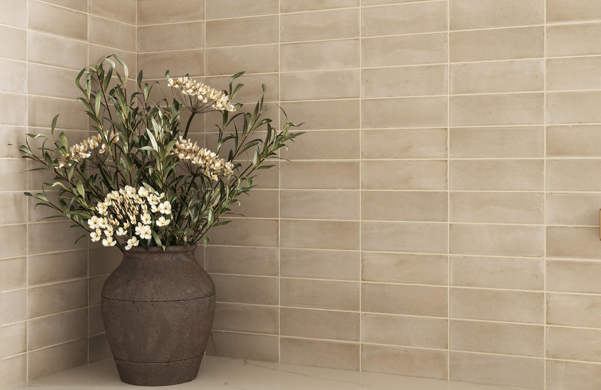 Beige subway tile wall in a kitchen corner with soft tonal variation, white grout, a marble countertop, and a dark ceramic vase with flowers.