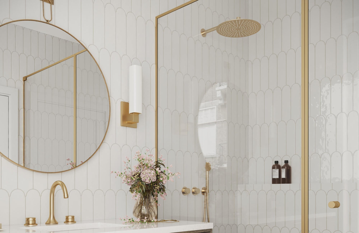 Elegant bathroom with white scalloped wall tiles, accented by brushed gold fixtures, a round mirror, and vertical sconces.