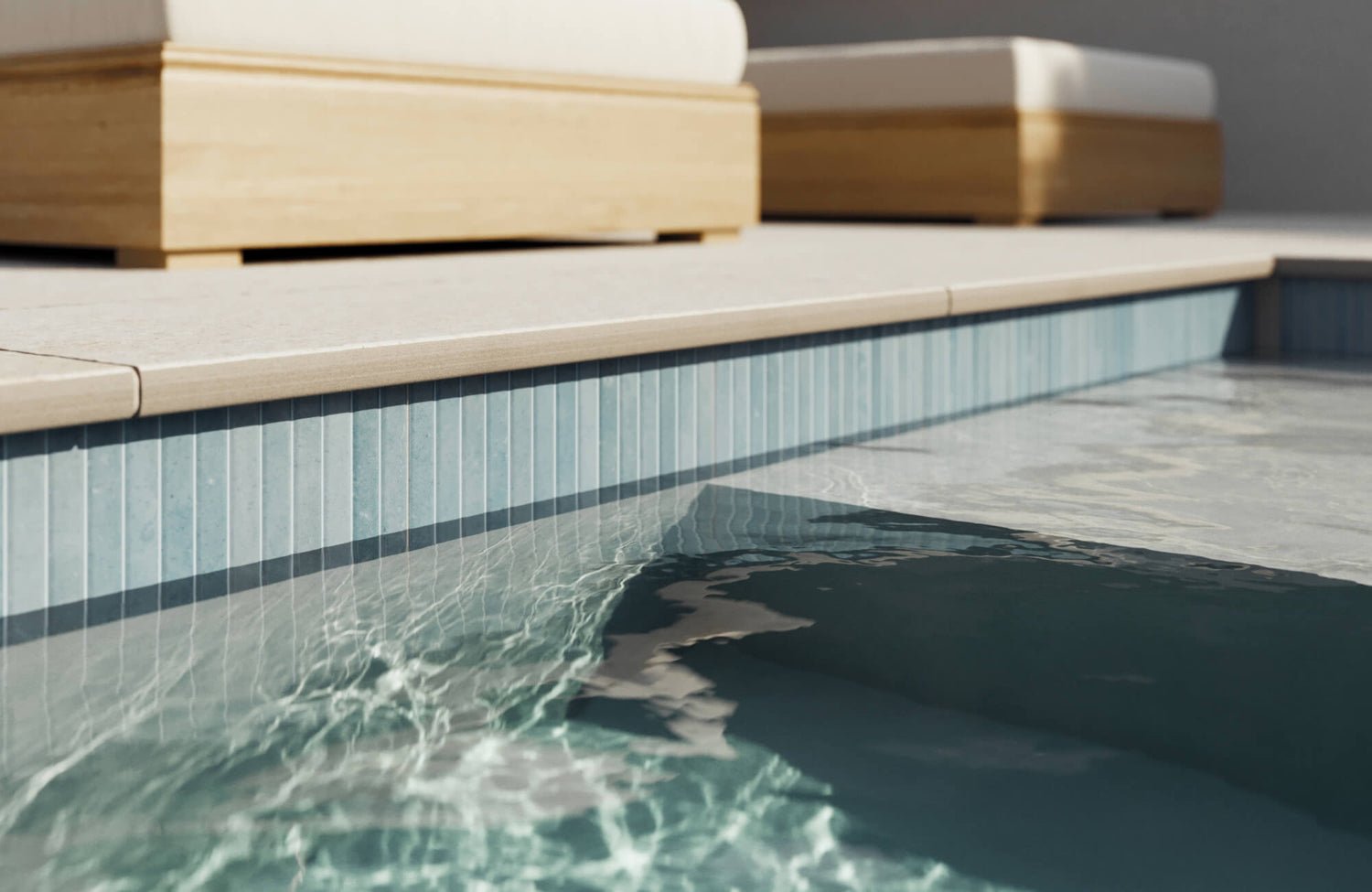 Elegant vertical pool tiles in soft sky blue create a serene, spa-like edge beneath sun-drenched stone decking.