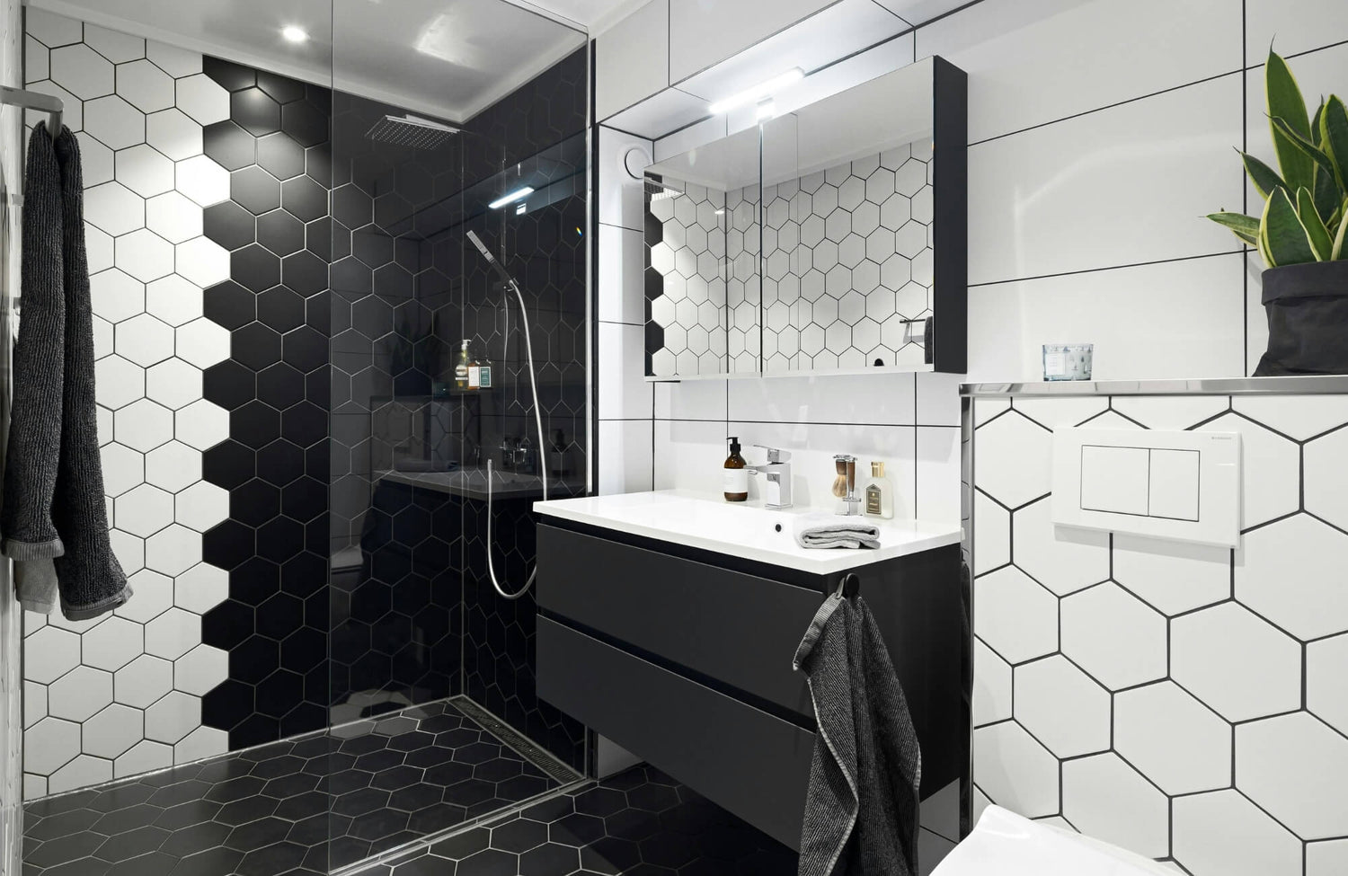 Modern bathroom featuring black and white hexagon tiles, a glass shower enclosure, floating vanity, and minimalist decor.