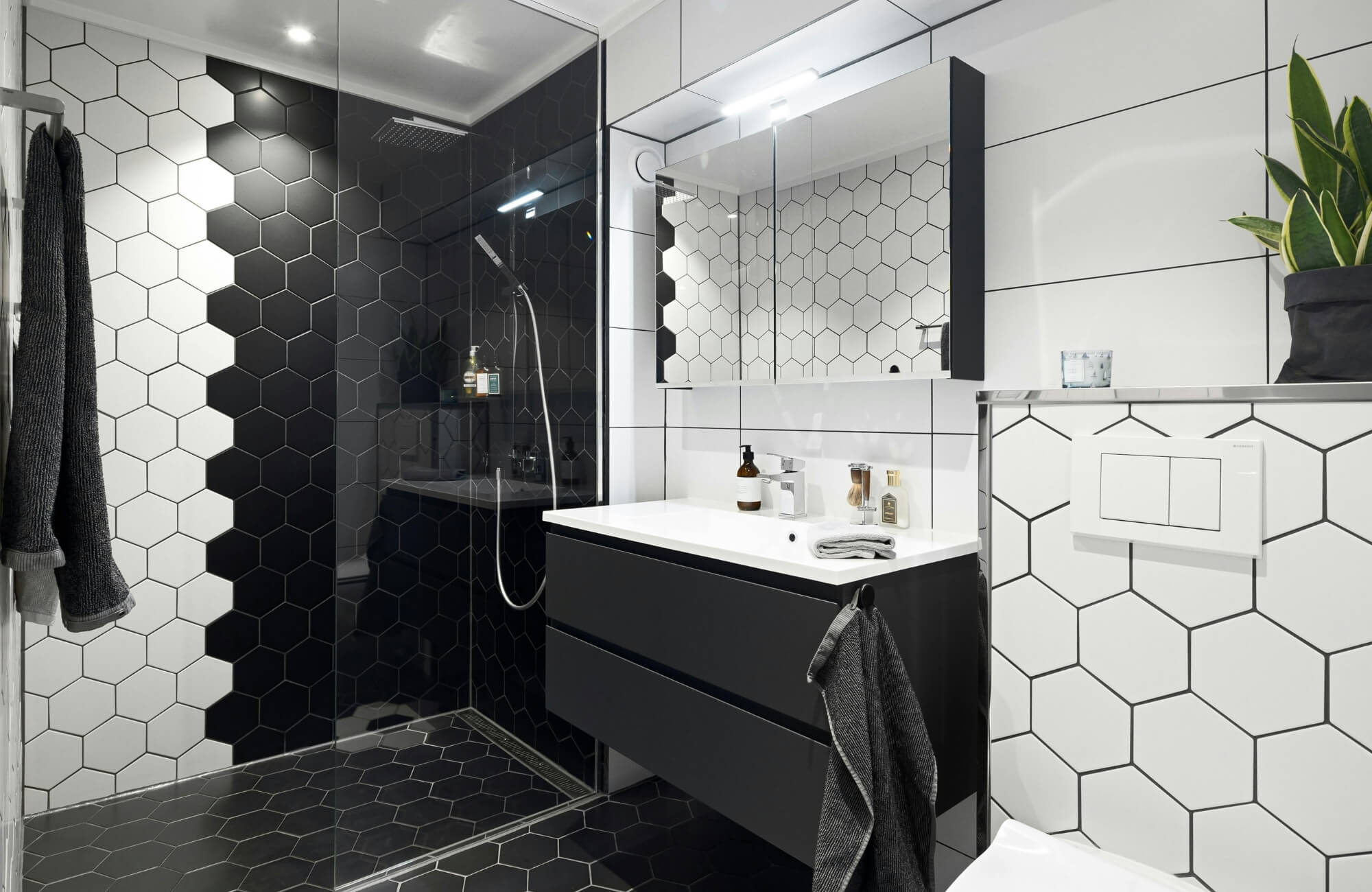 Modern bathroom featuring black and white hexagon tiles, a glass shower enclosure, floating vanity, and minimalist decor.