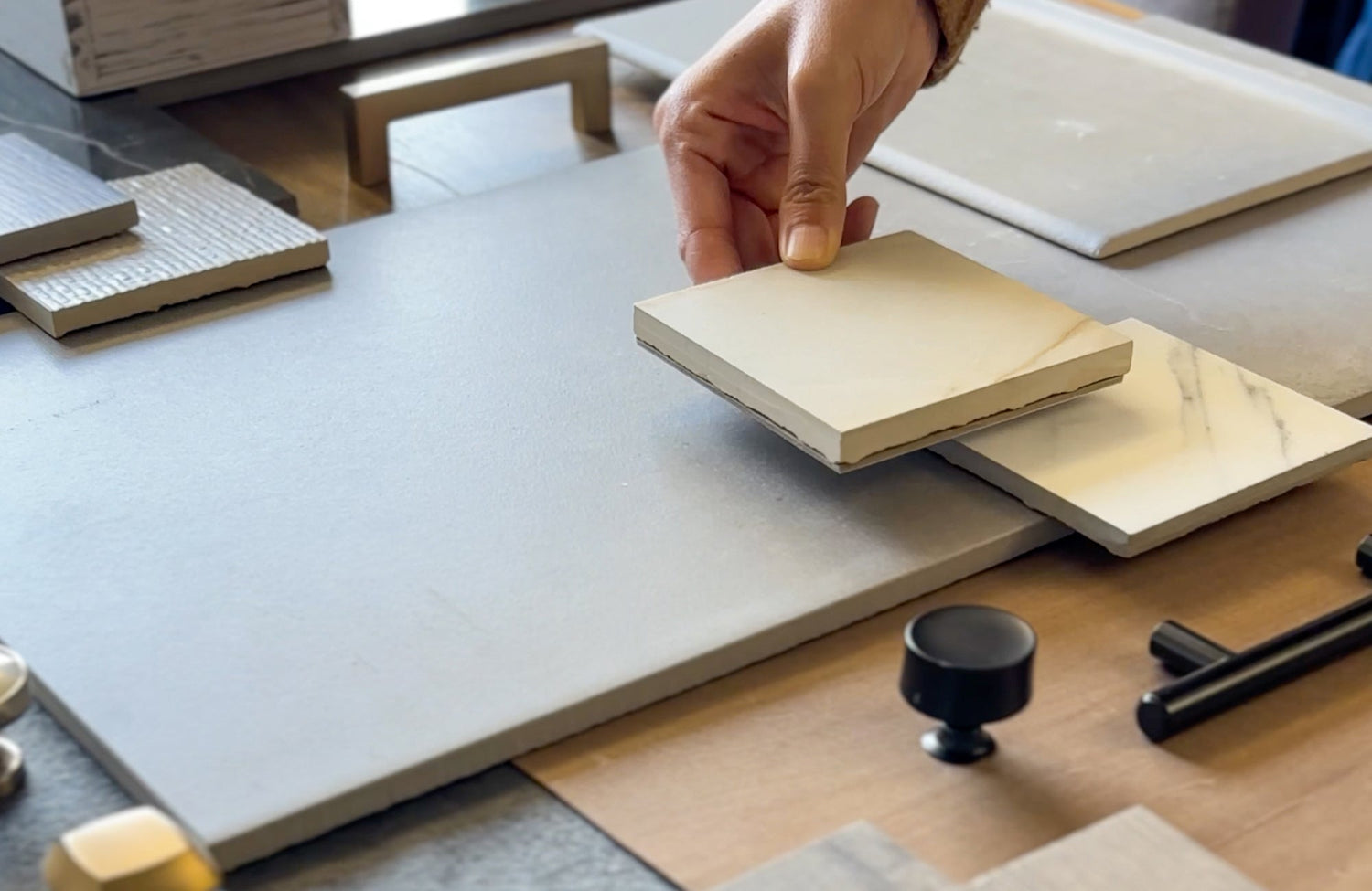 Close-up of tile samples being layered over countertop surfaces, illustrating how color, veining, and finish comparisons work when selecting materials for a space.