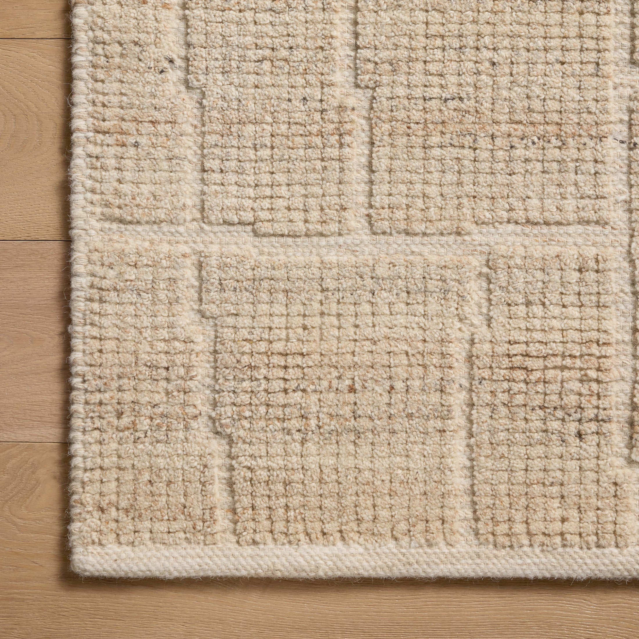 A close-up view of a warm beige wool-cotton blend rug, revealing a textured surface and subtle rectangular pattern created through a tightened, flattened weave.