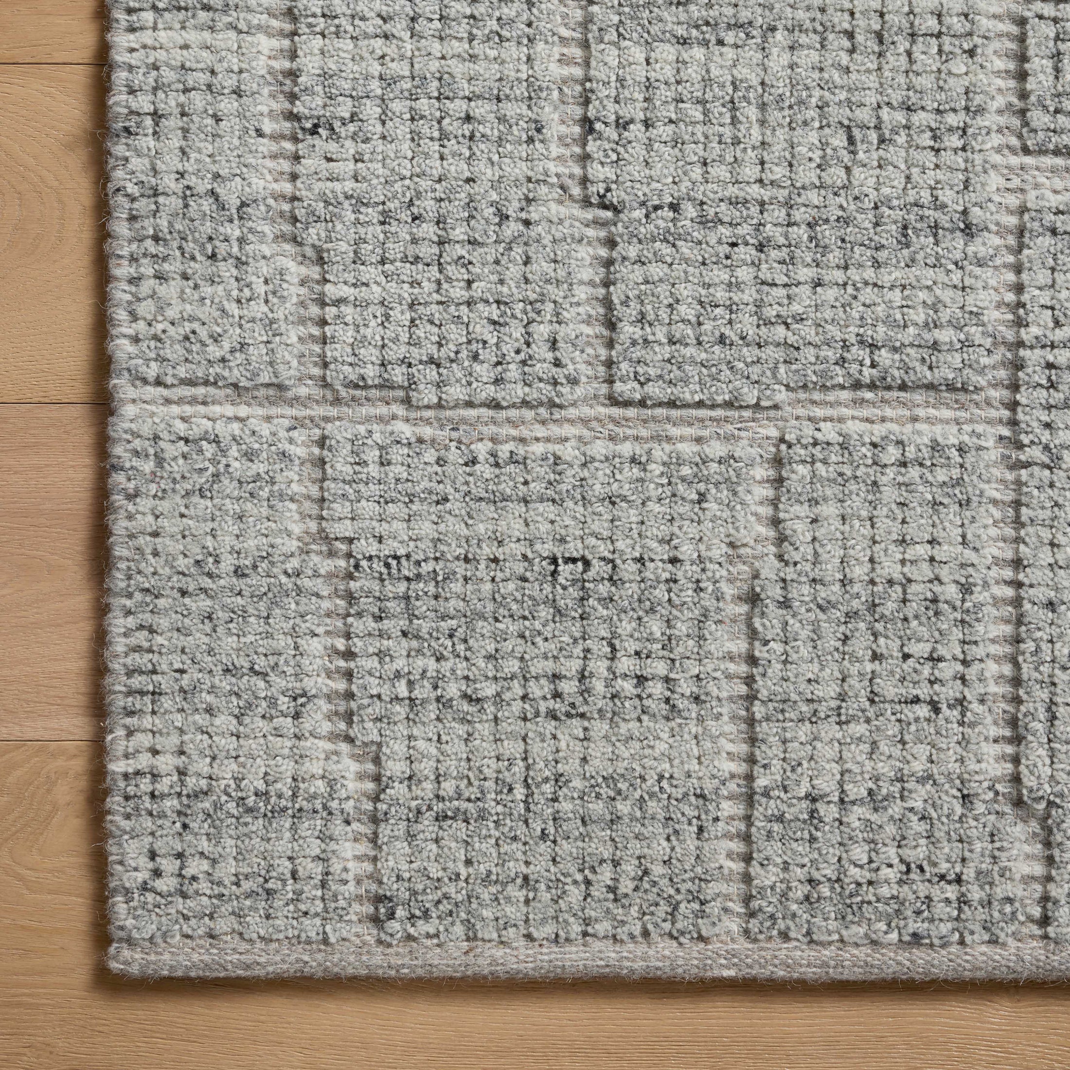 This detailed view highlights a bluish gray rug with subtle rectangular linework emerging from a flattened weave, revealing its hand-loomed, artisanal texture.
