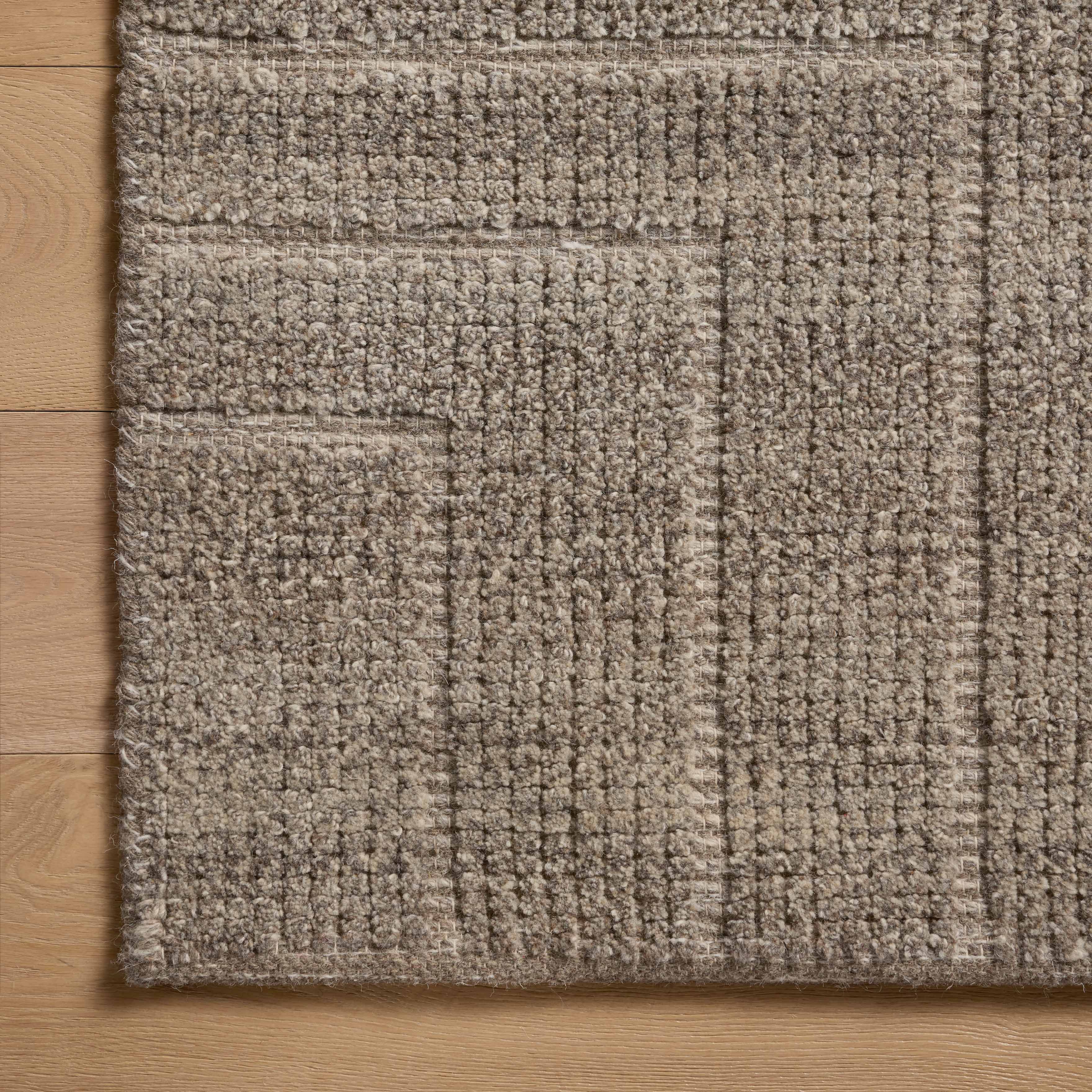 A close-up view of a brown rug with a dense, hand-loomed texture, showing subtle tonal shifts and angular lines that create a softly geometric pattern.