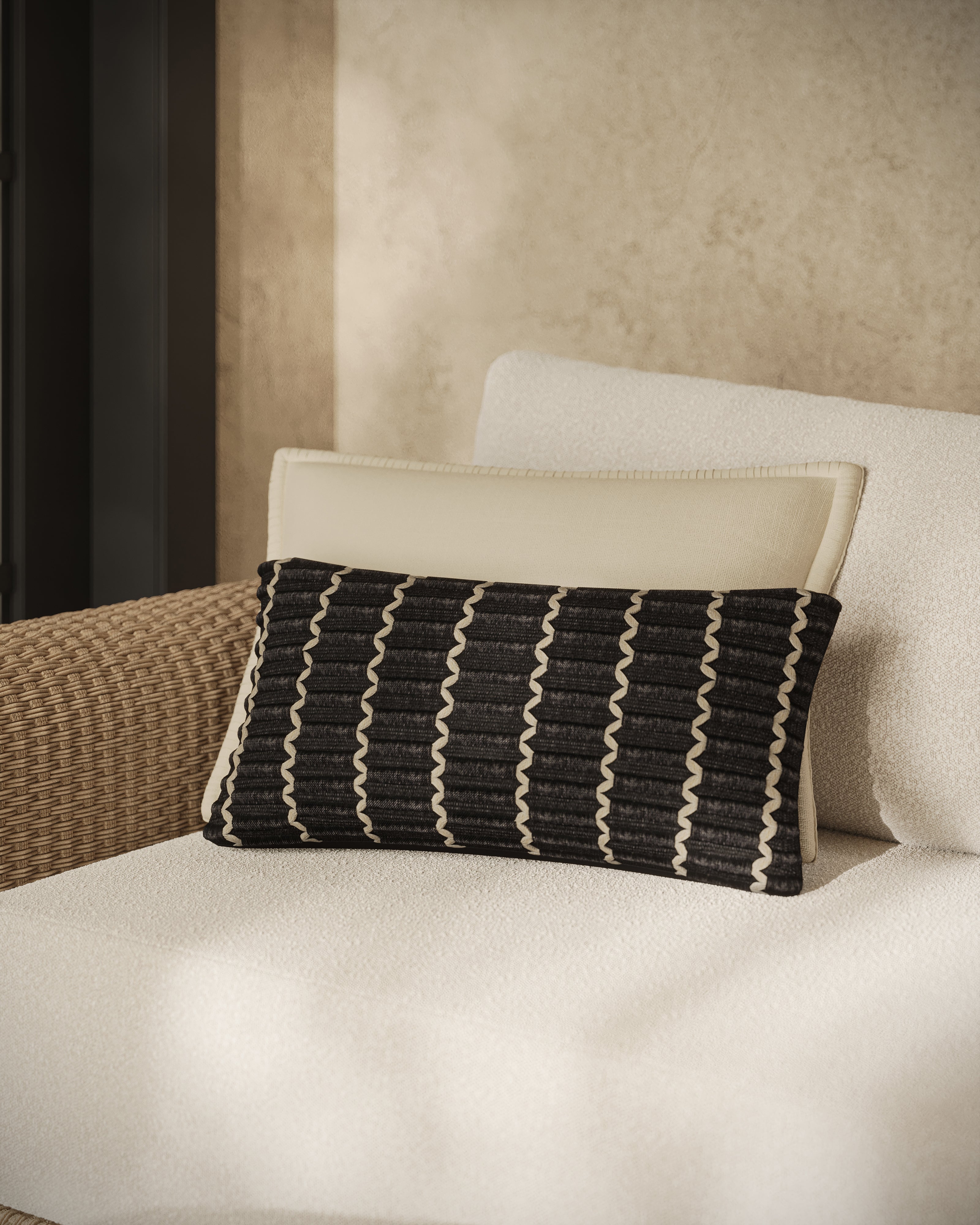 Black Marisette 12 x 27 lumbar pillow styled on a neutral sofa, featuring raised dark weave with white linear loops and a refined knife-edge silhouette.